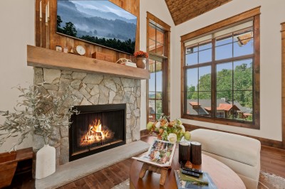 Tall windows stretch to the peak of the vaulted ceiling, framing neighboring rooftops and layered ridgelines beyond the fire — a bright, book-filled corner made for settling in with coffee.