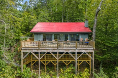 A charming mountain cabin with a striking red metal roof sits elevated among lush trees, offering privacy and sweeping forest views. The wraparound deck invites peaceful mornings surrounded by fresh mountain air.