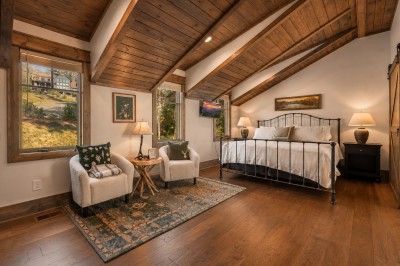 Unwind beneath soaring wood-beamed ceilings in this vaulted bedroom, complete with a fireside-style seating nook for your morning coffee and windows that frame the tree-lined mountainside in every direction.