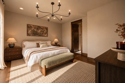 Warm natural light fills this elegant king bedroom, where a wrought-iron chandelier and rustic wood door frame lead straight to the en suite bath. Understated, calm, and beautifully lit.