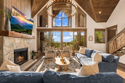 Gather in the vaulted great room beneath soaring wood-beamed ceilings, where a floor-to-ceiling stone fireplace anchors the space and walls of windows frame breathtaking mountain views. Sink into the plush sectional and settle in for the evening