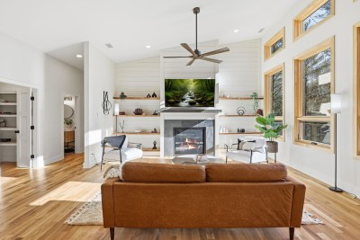Unwind in this bright, open living room where floor-to-ceiling windows flood the space with natural light. Cozy seating, a fireplace, and serene views invite slow mornings, movie nights, and effortless togetherness.