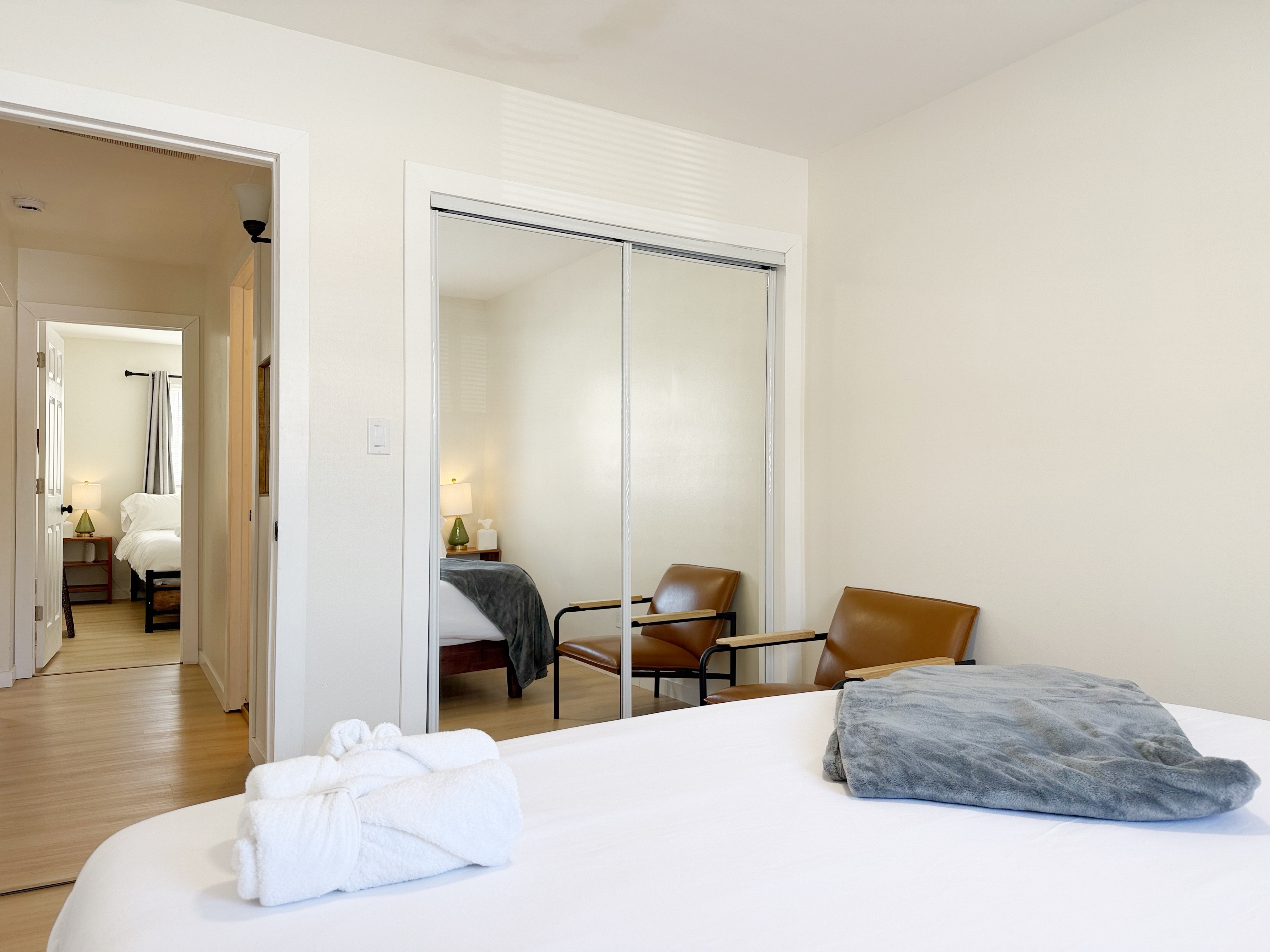 Sunny minimalist bedroom with mirrored closet and cozy leather seating.