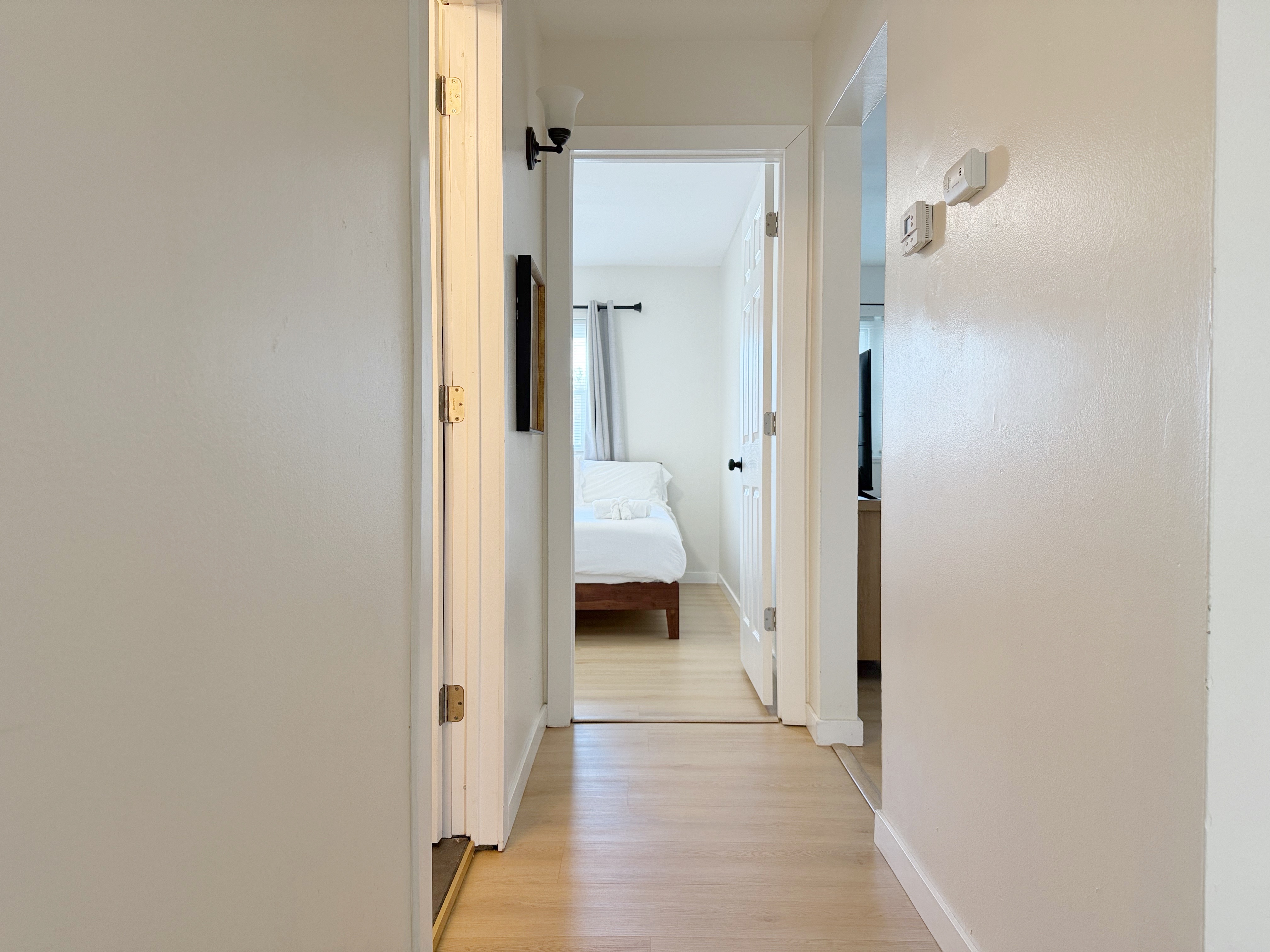 Bright, airy hallway to a sunlit bedroom with light-wood floors.