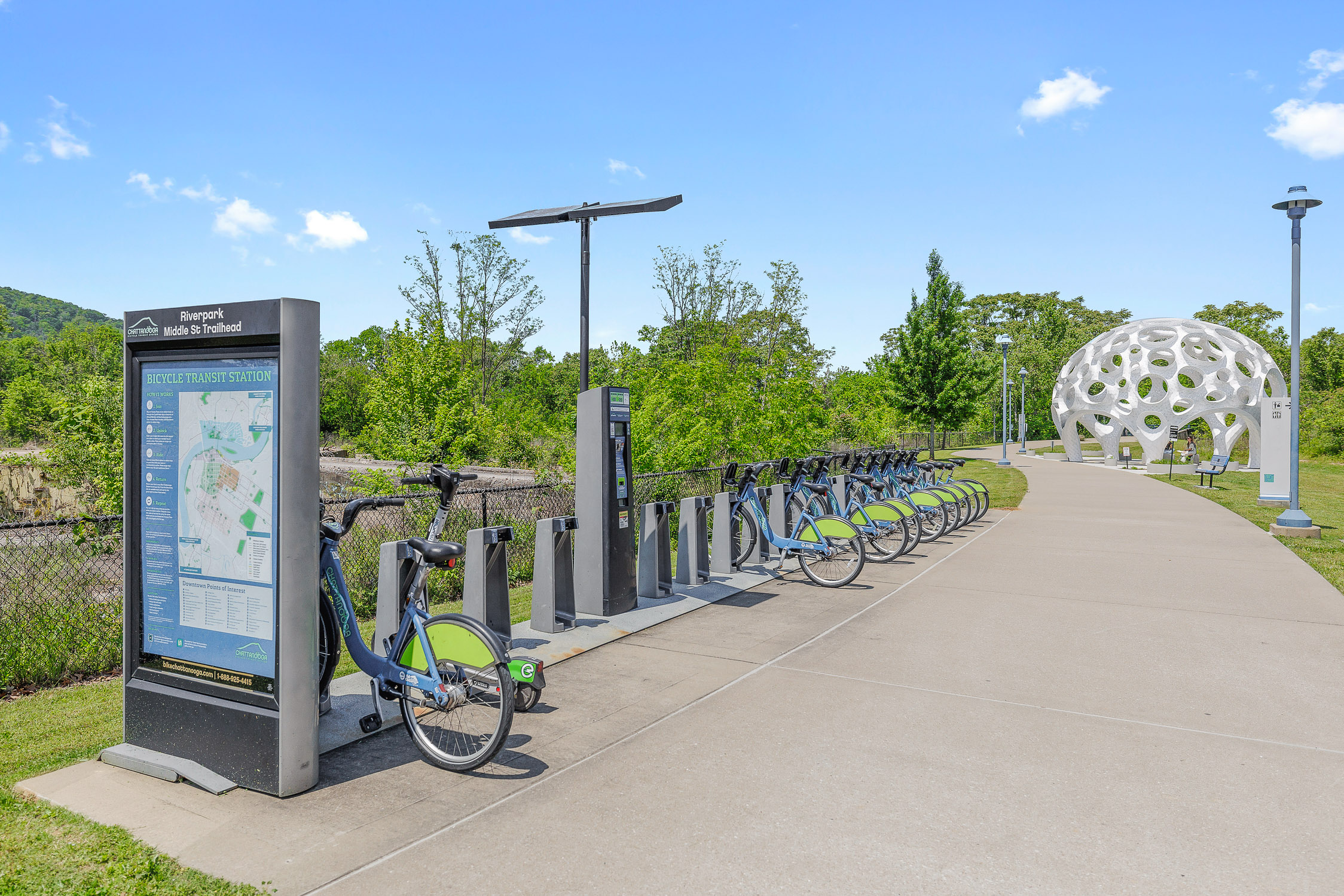 Bike-share station along a scenic riverside trail with modern pavilion