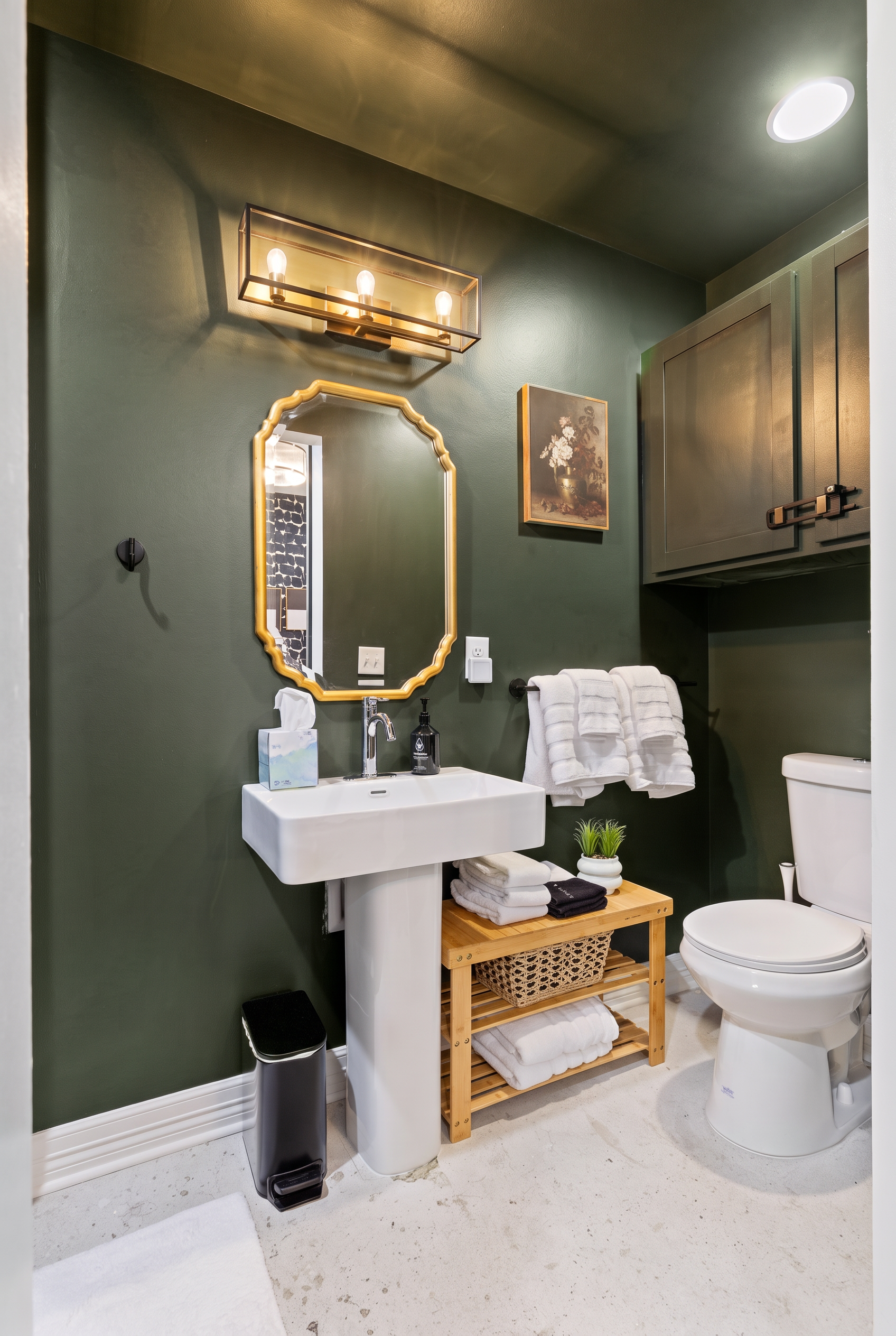 Elegant bathroom with moody green walls, luxe lighting, and stocked towel storage