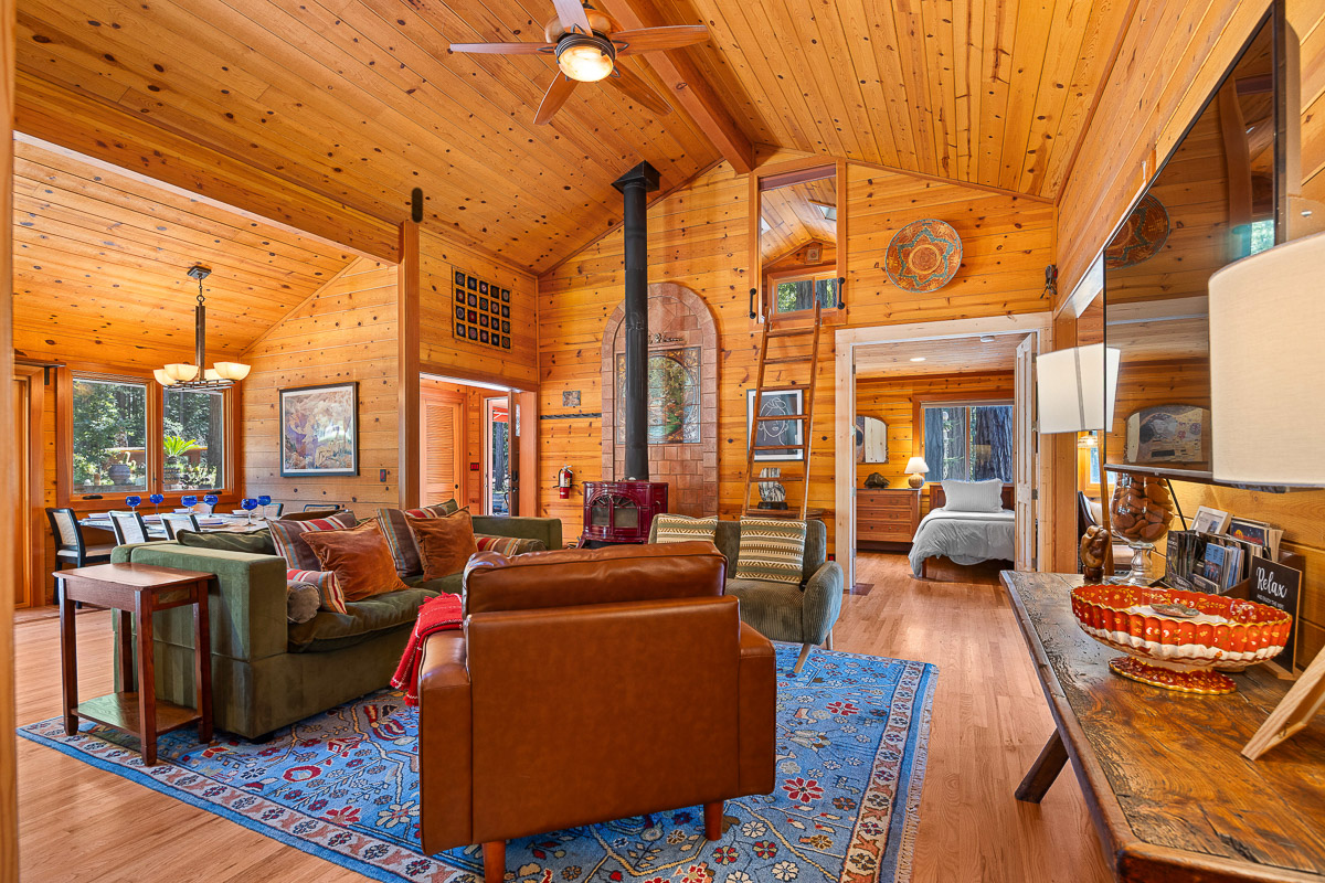 Sunny vaulted cabin living room with wood stove, loft, and open dining.