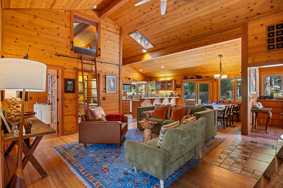 Sunny wood-clad great room with loft, island kitchen, and forest views