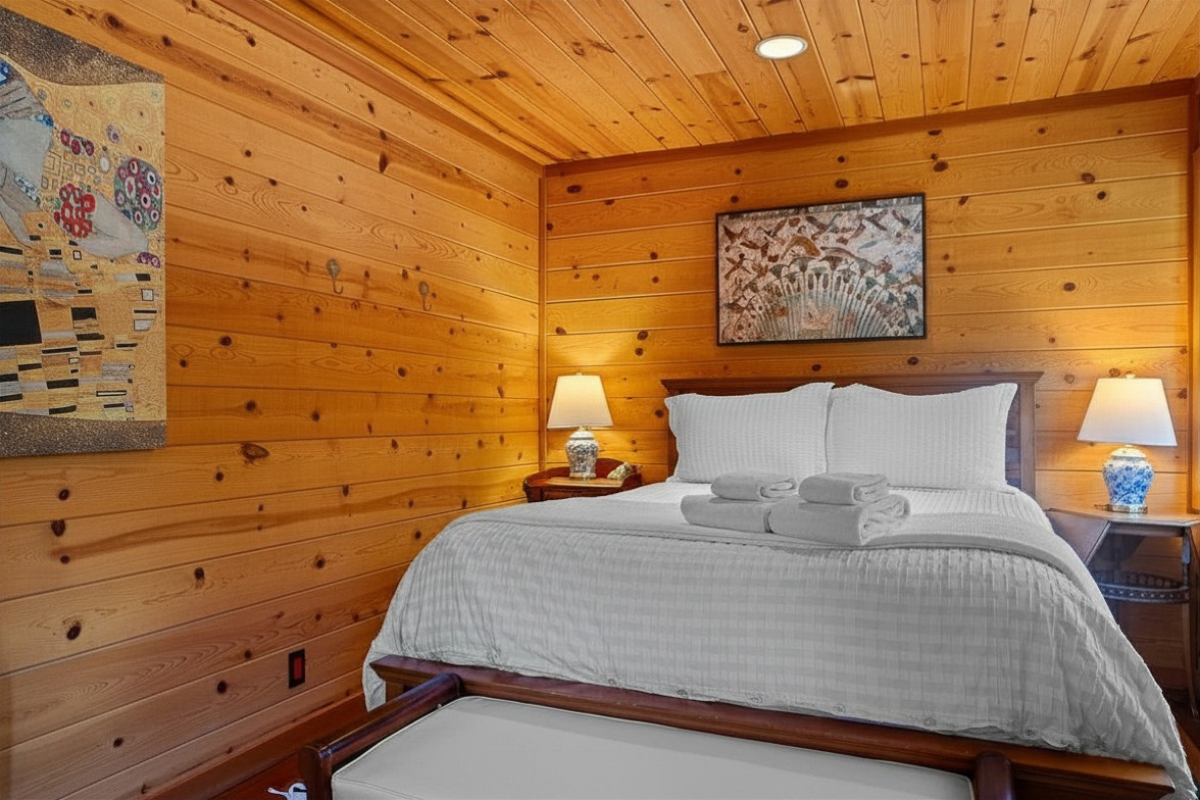 Cozy wood-paneled bedroom with king bed, crisp linens, warm lamplight.