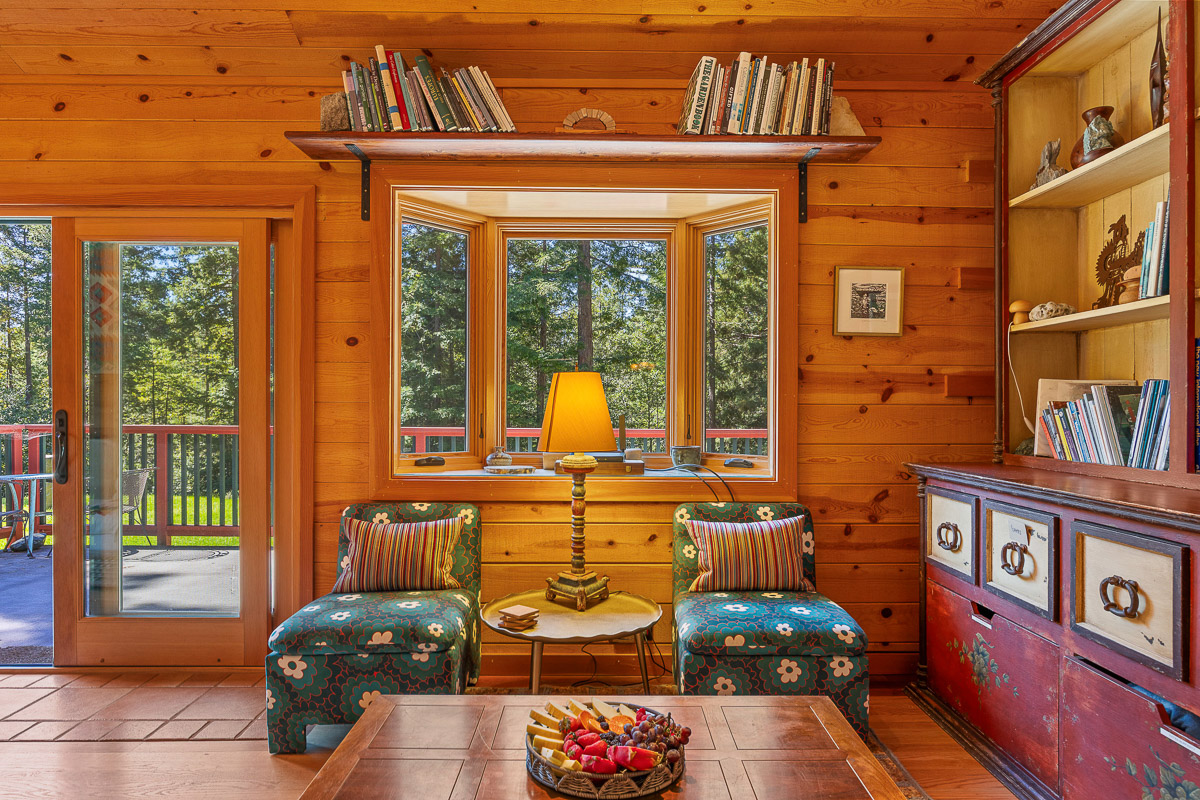 Cozy cabin window nook with forest views and deck access—ideal reading spot.