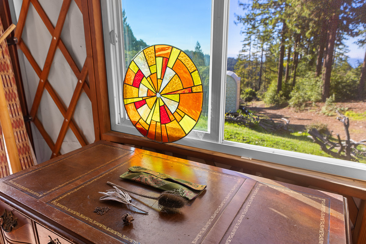 Stained-glass sun catcher and forest view—serene, rustic workspace