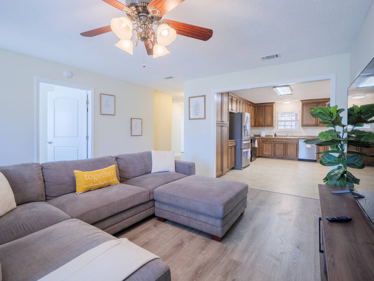 Living room with gray sectional and yellow pillows, kitchen beyond