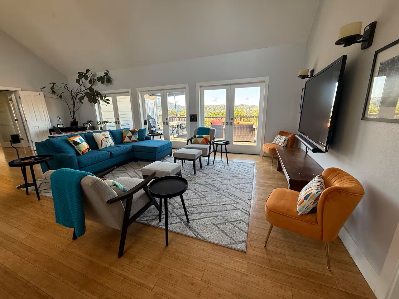 Bright lounge with large TV, teal sectional, and doors to a view deck.