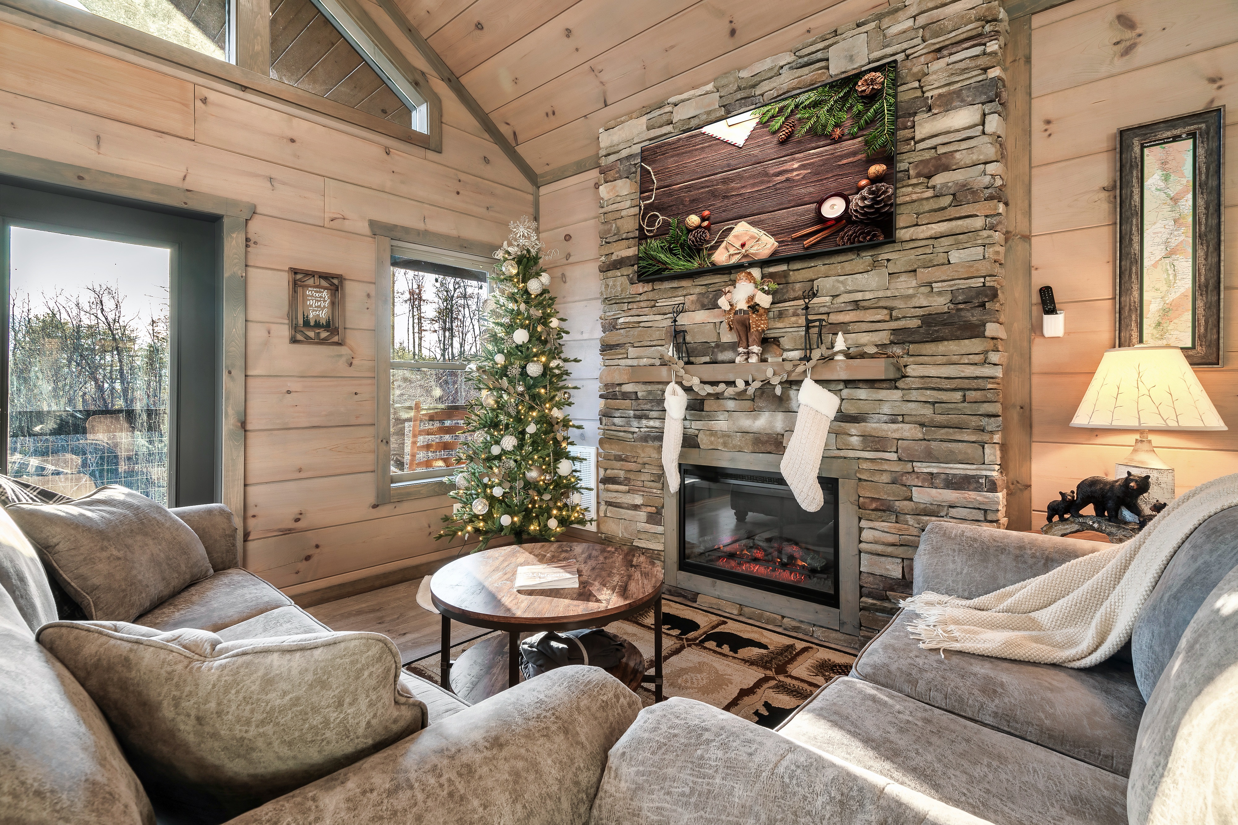 Cozy cabin living room with stone fireplace, forest views, and festive charm