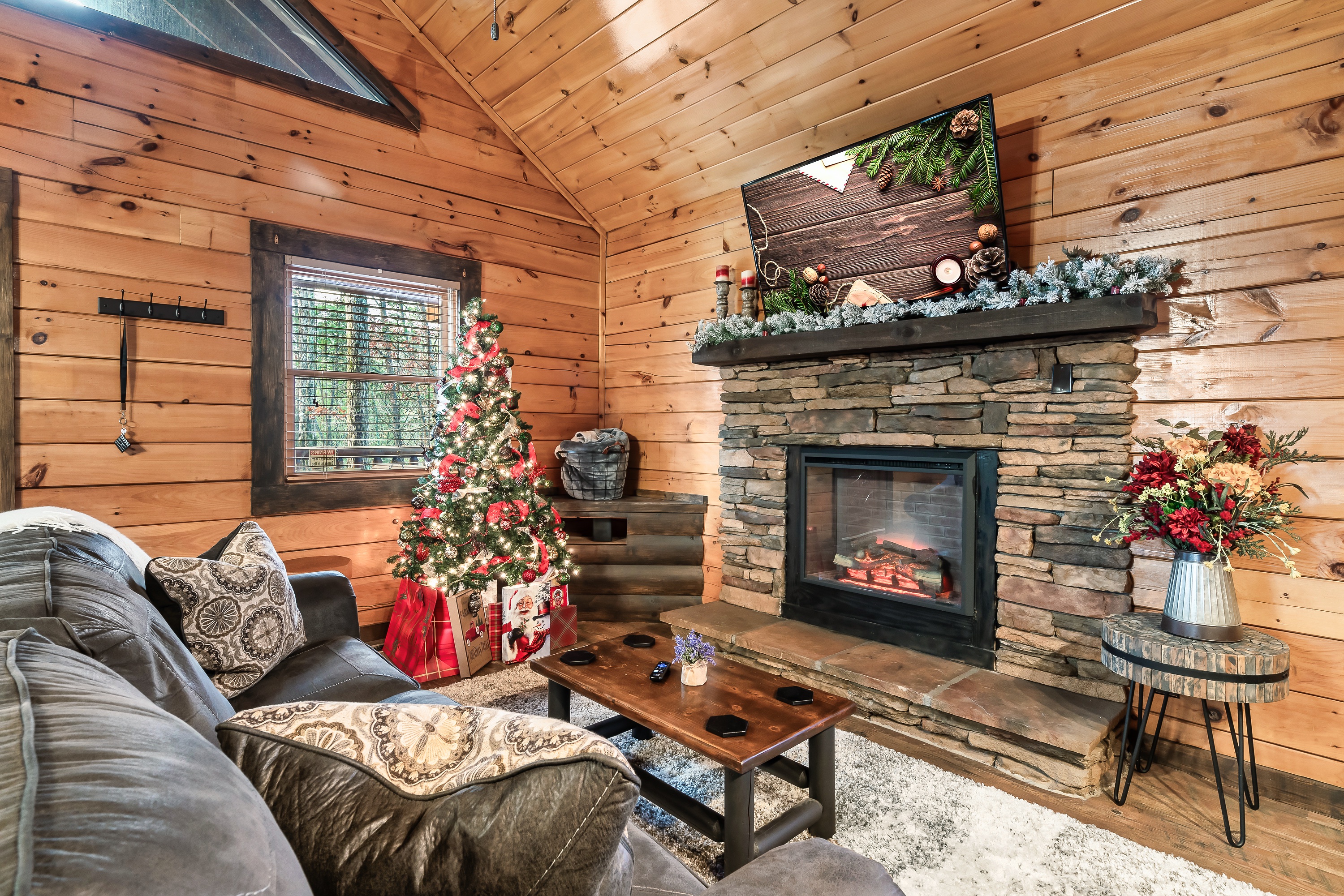 Living room dressed for the holidays, with the tree lit beside the stone fireplace