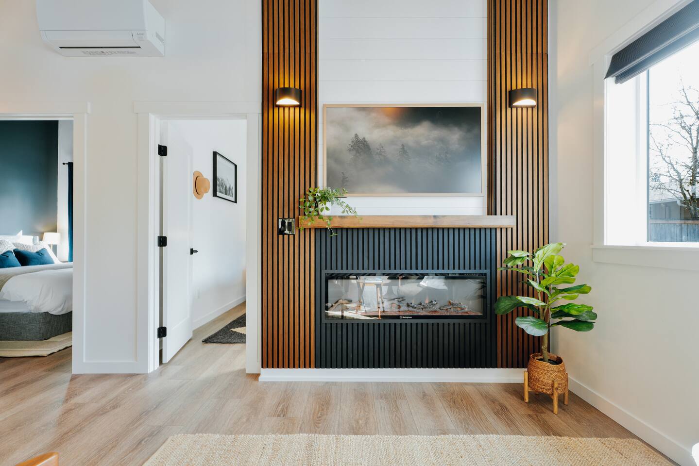 The living room, a floor-to-ceiling wood slat feature wall, electric fireplace, and a sunny seating area.