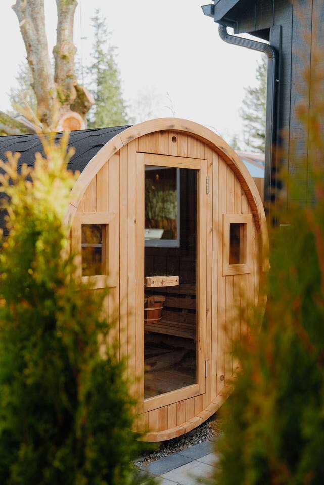 A Redwood Outdoors barrel sauna set among evergreen trees in the backyard.