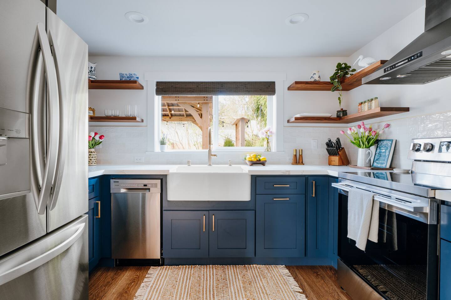 The finished kitchen, navy shaker cabinets, a farmhouse sink, white quartz counters and walnut floating shelves.