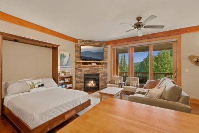 This studio pairs a queen Murphy bed with a dining table and fireside sitting area, floor-to-ceiling windows framing the Blue Ridge treeline and a private balcony just steps away — flexible living for however your group beds down.