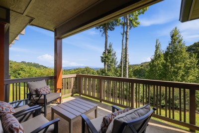Unwind on the covered balcony where deep-cushioned chairs and patterned pillows invite you to linger over coffee while layered Blue Ridge peaks unfold past the treeline, an ever-changing backdrop from morning haze to golden-hour glow.