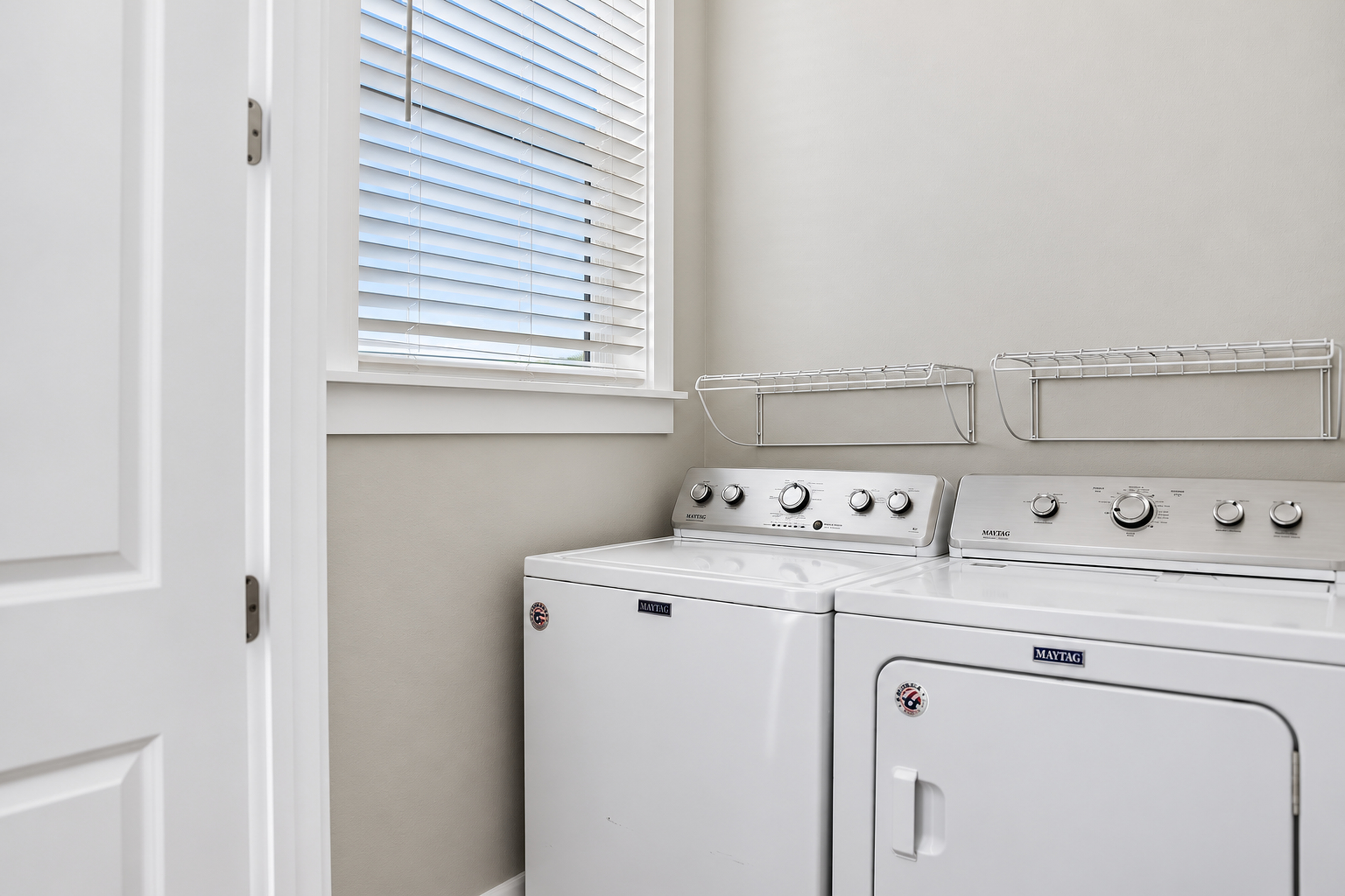 Bright laundry room with full-size washer, dryer, and handy storage shelves