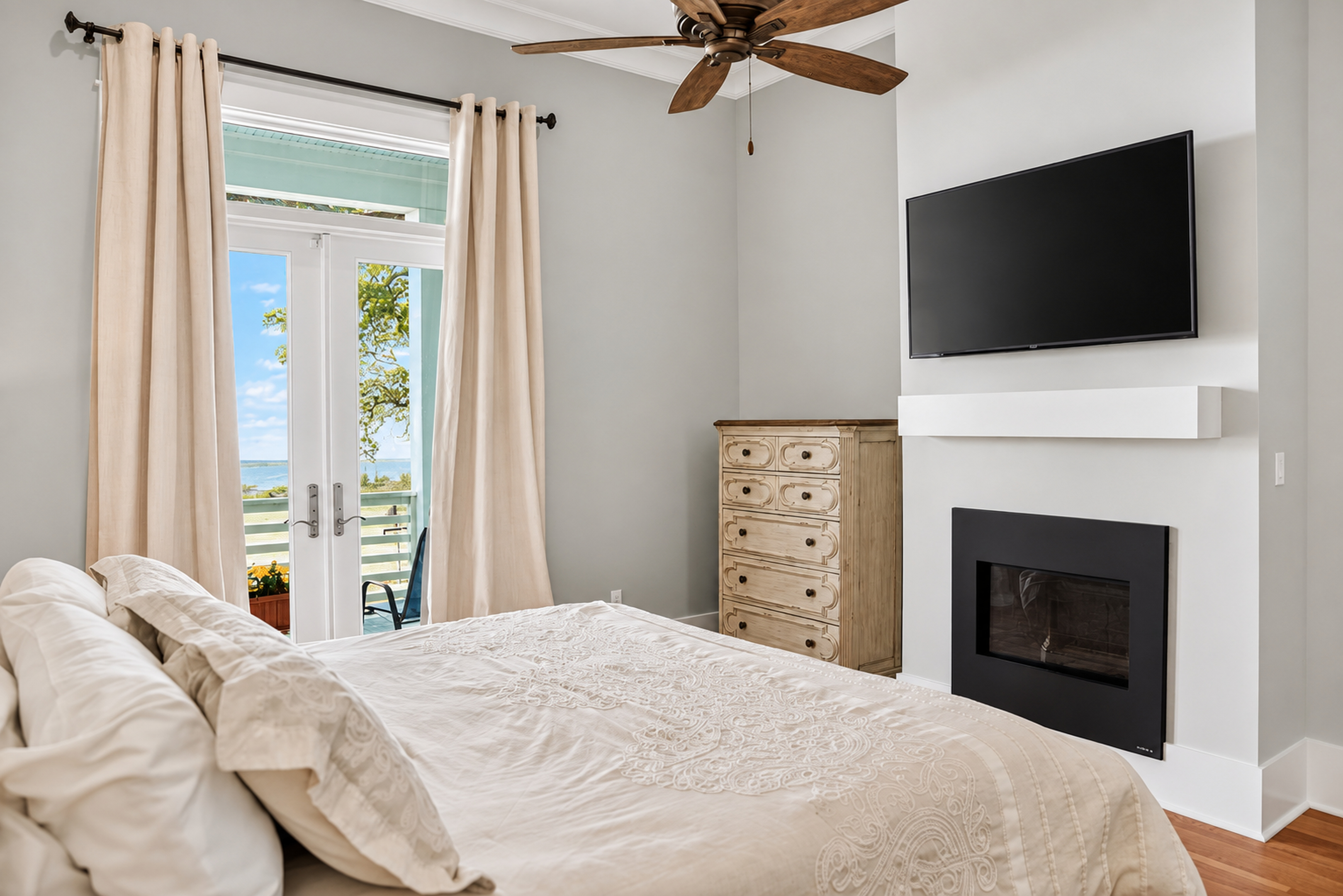 Bright bedroom with fireplace, TV, and private balcony water views