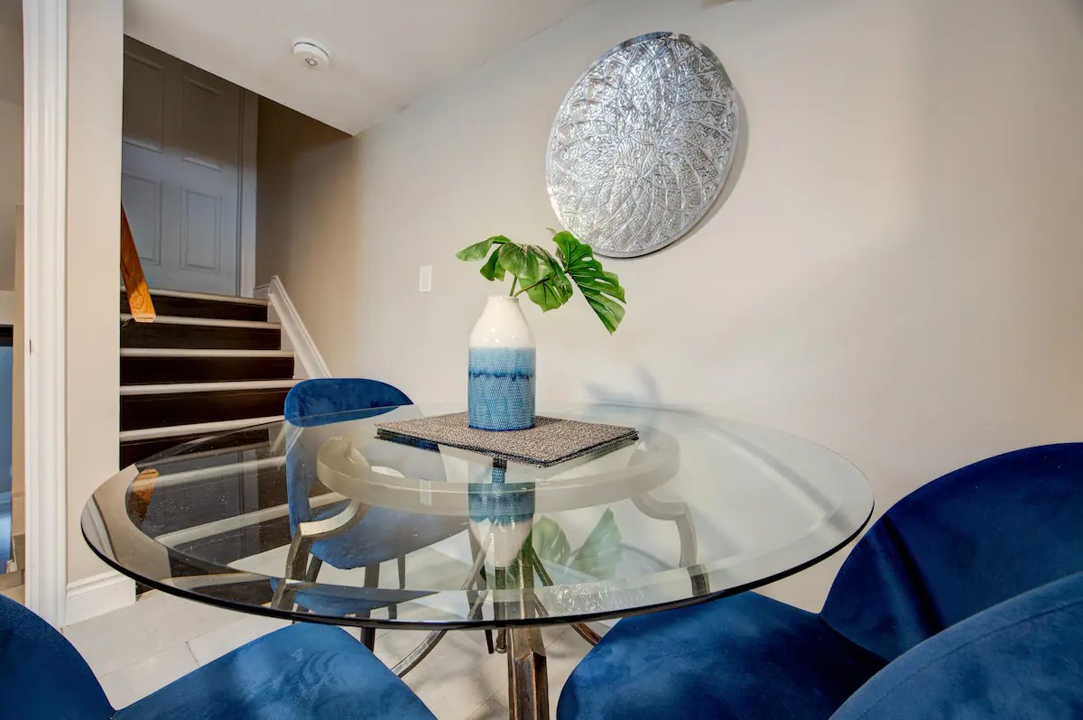 Chic dining nook with glass table, blue velvet chairs, and modern art