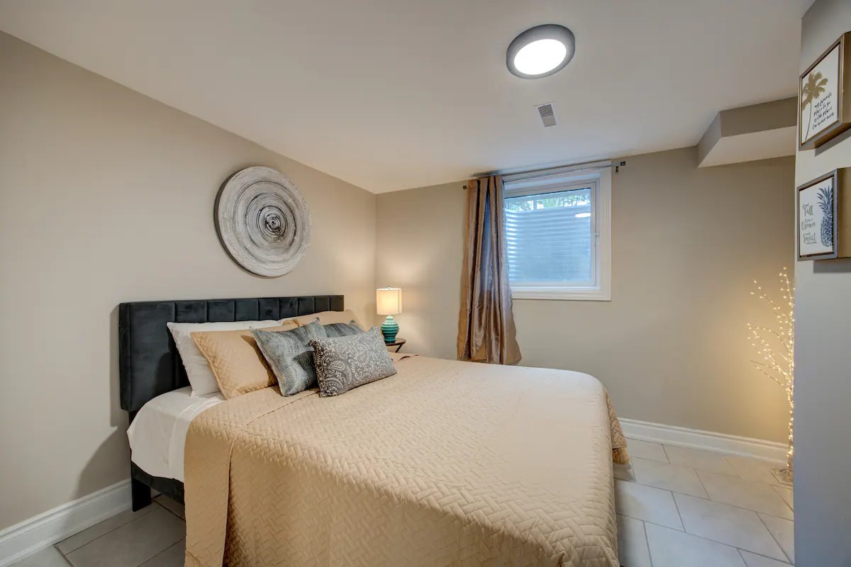 Cozy neutral bedroom with queen bed, soft lighting, and window light