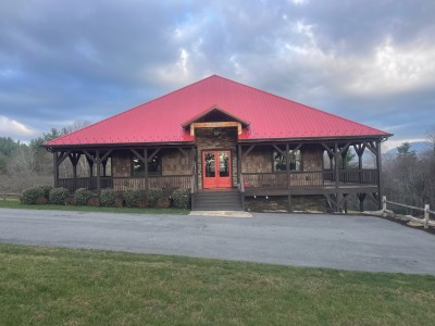Rustic lodge with red roof, wraparound porch & mountain views