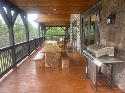Covered deck with grill, live-edge table, and forest-view rockers