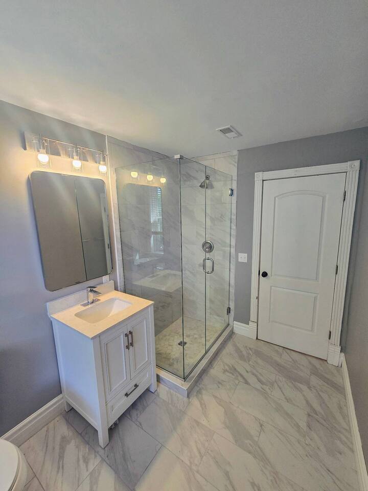 Bright and clean bathroom with a walk-in shower, modern vanity, and marble-style tile throughout.