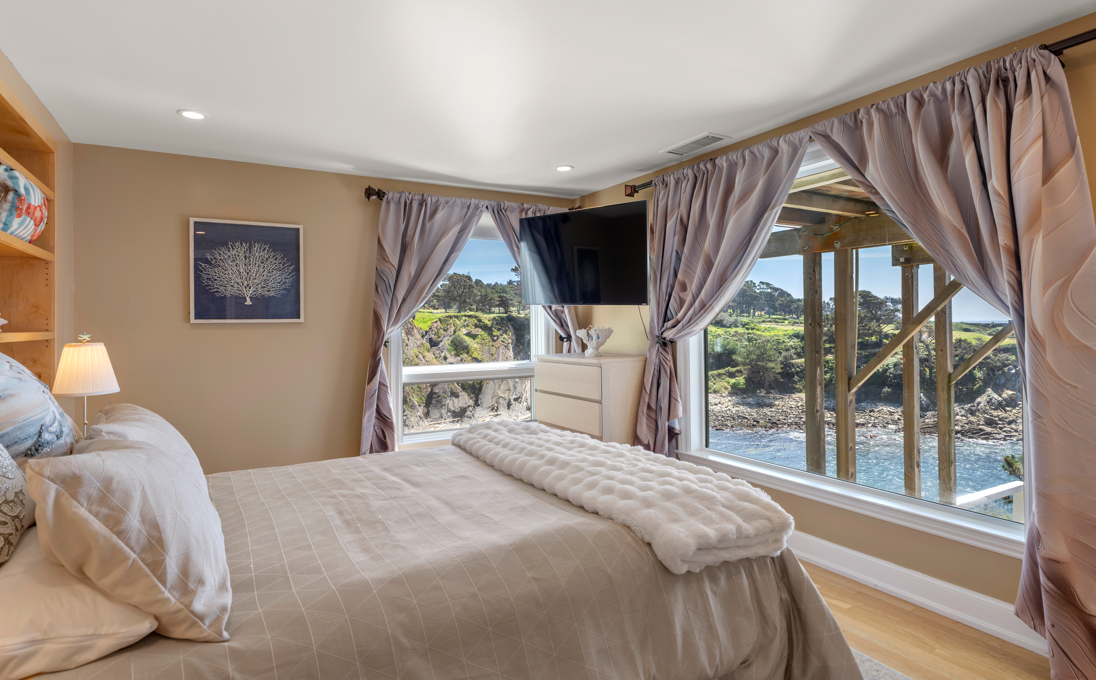 Oceanfront bedroom with panoramic windows, TV, and serene coastal views