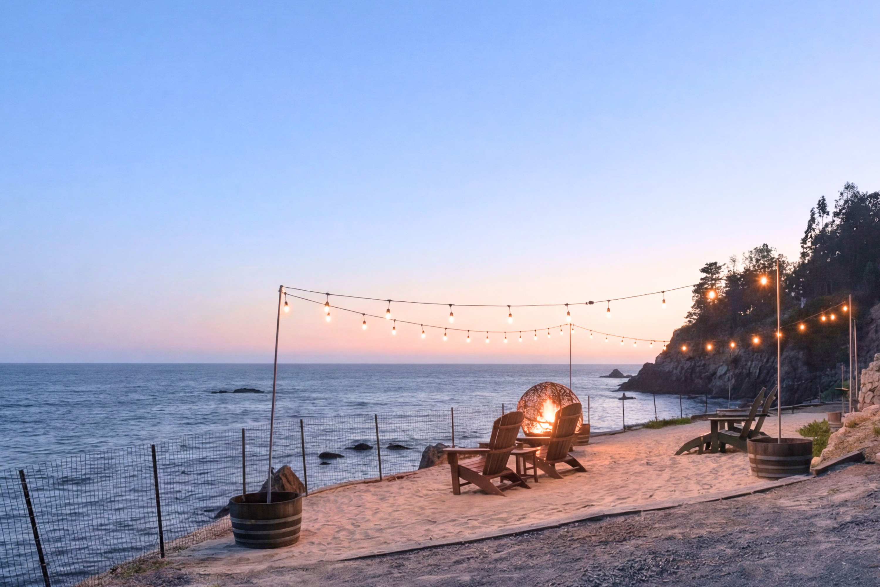 Cliffside beach lounge with fire pit, string lights, and sunset ocean views