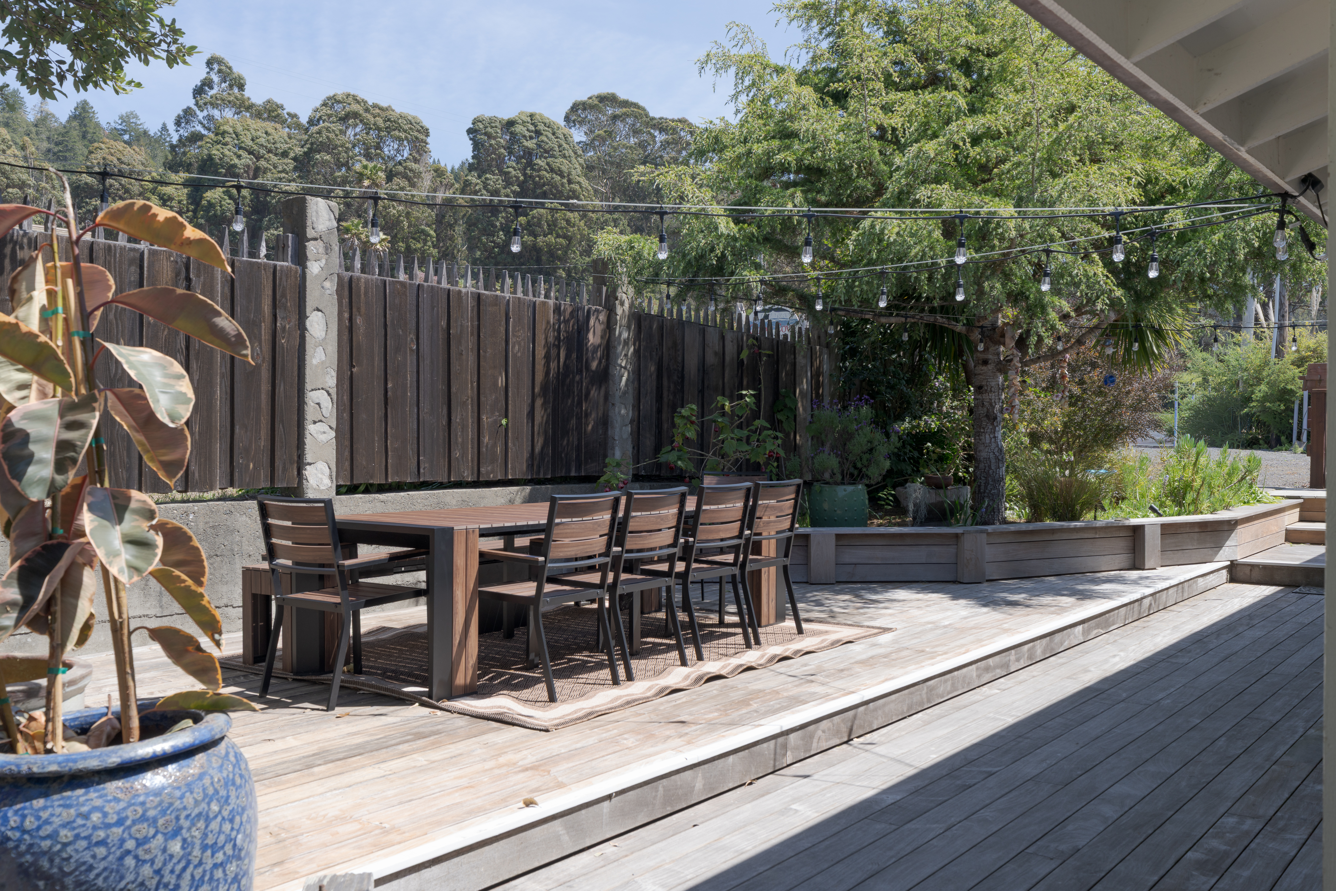 Sunny deck with dining set, string lights, and lush garden views.