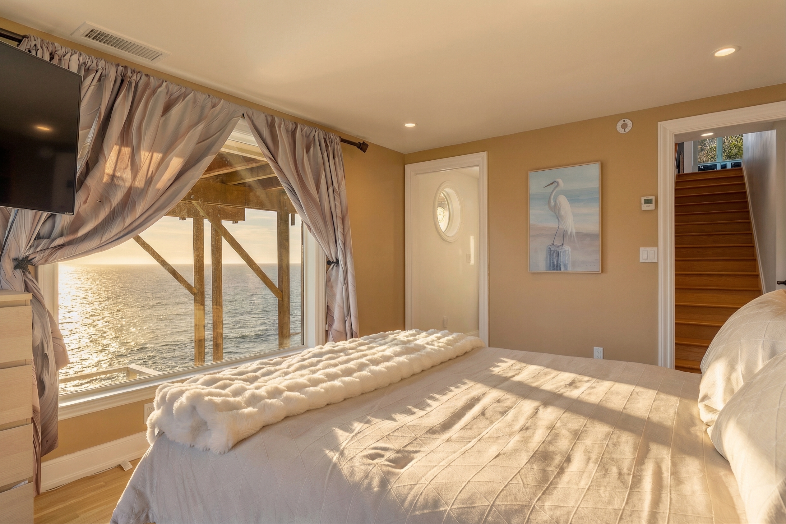 Oceanfront bedroom with sunset views, plush bedding, and TV