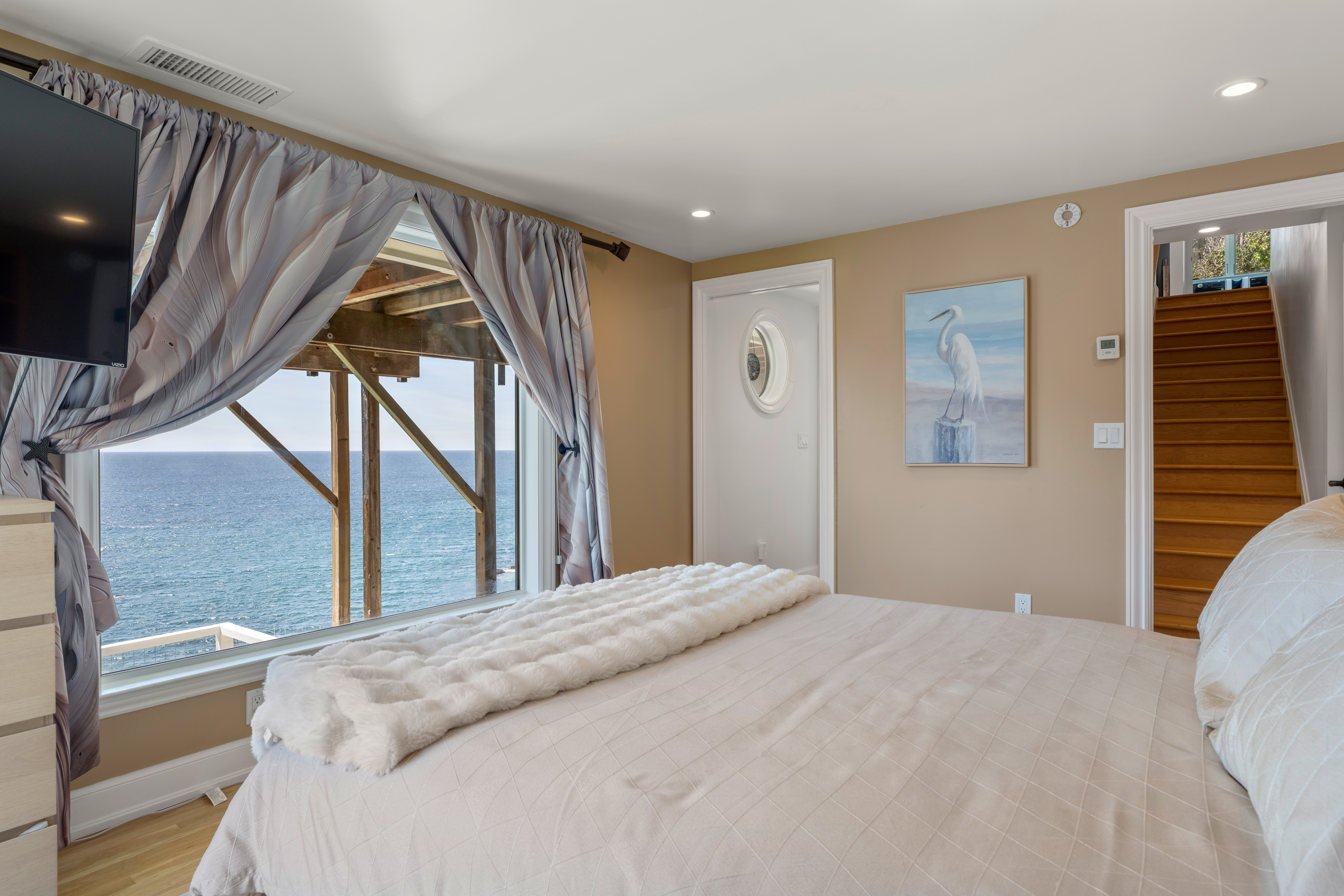 Oceanfront bedroom with panoramic views, TV, and serene coastal decor