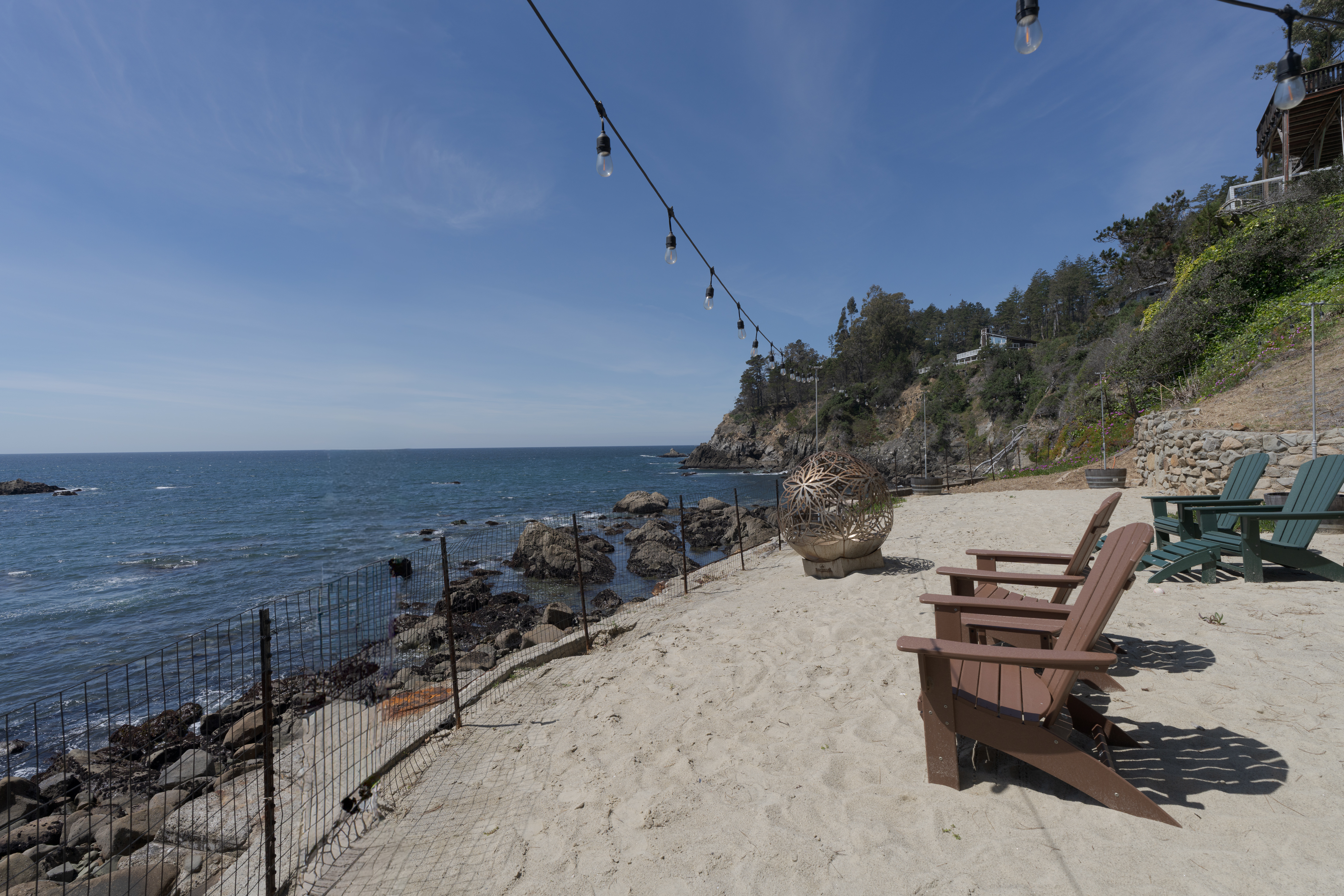 Private beachfront patio with Adirondack seating, fire pit, and cove views