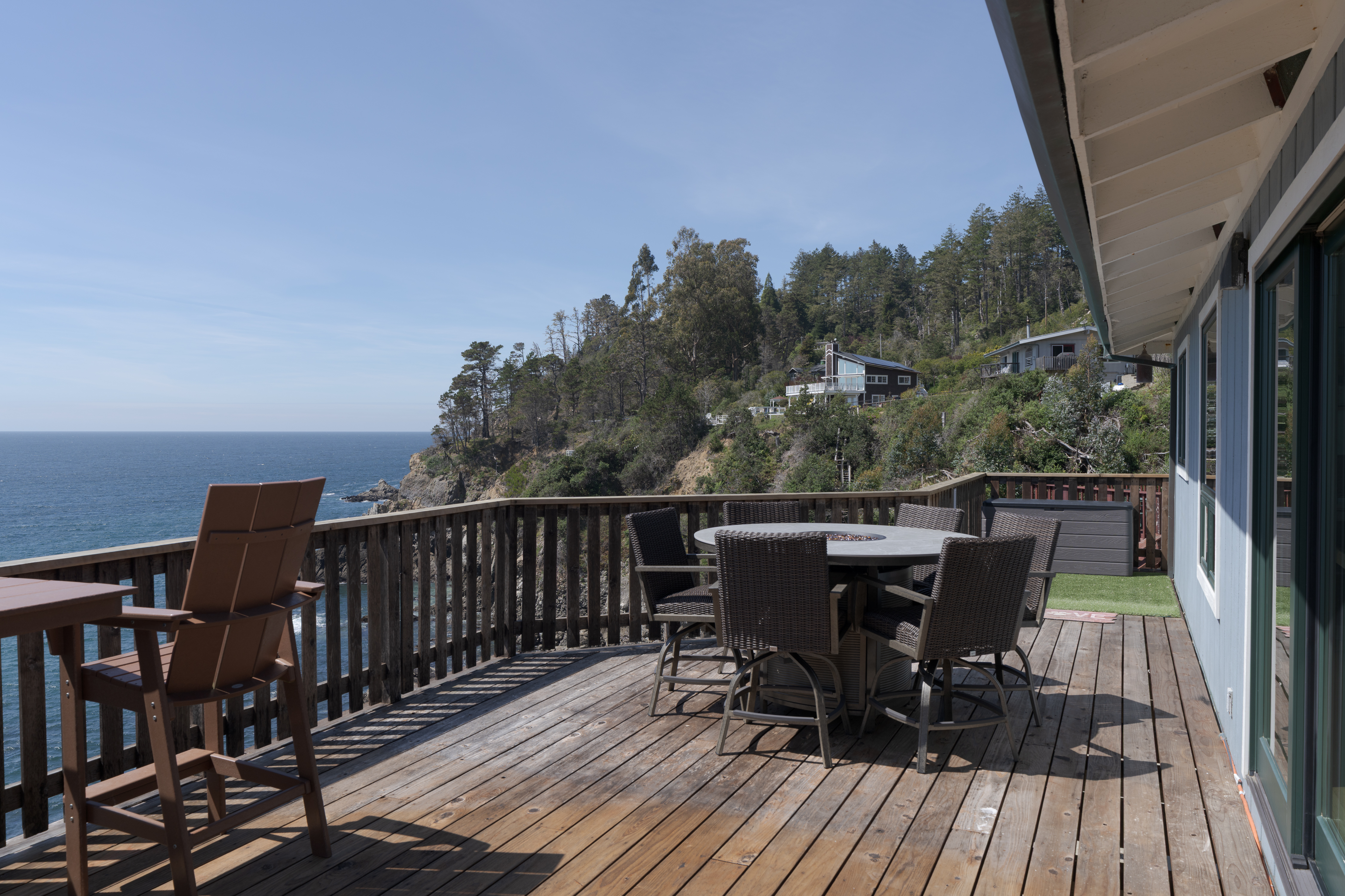 Expansive ocean-view deck with dining set and coastal hillside scenery