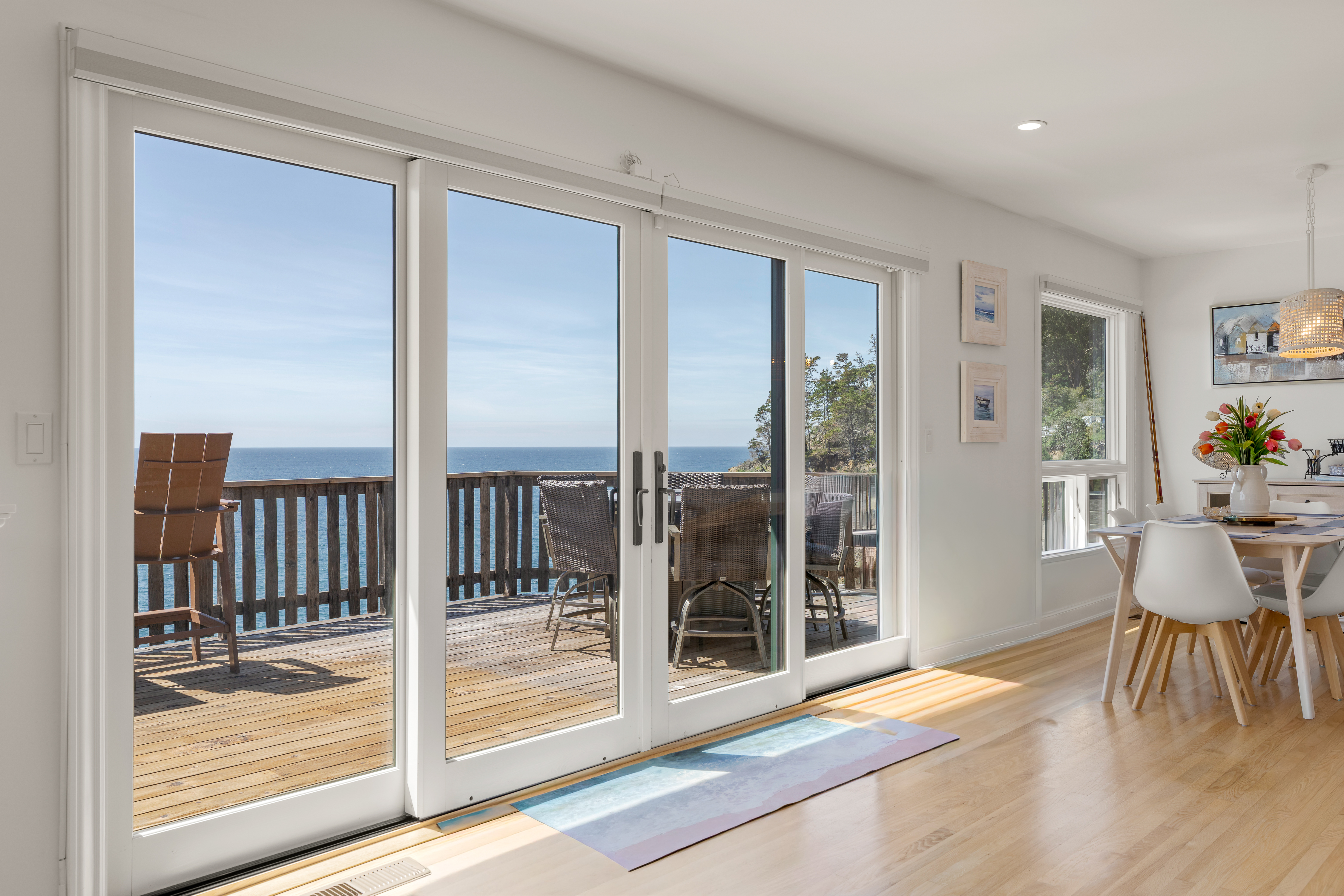 Bright coastal dining with ocean-view deck and floor-to-ceiling doors.