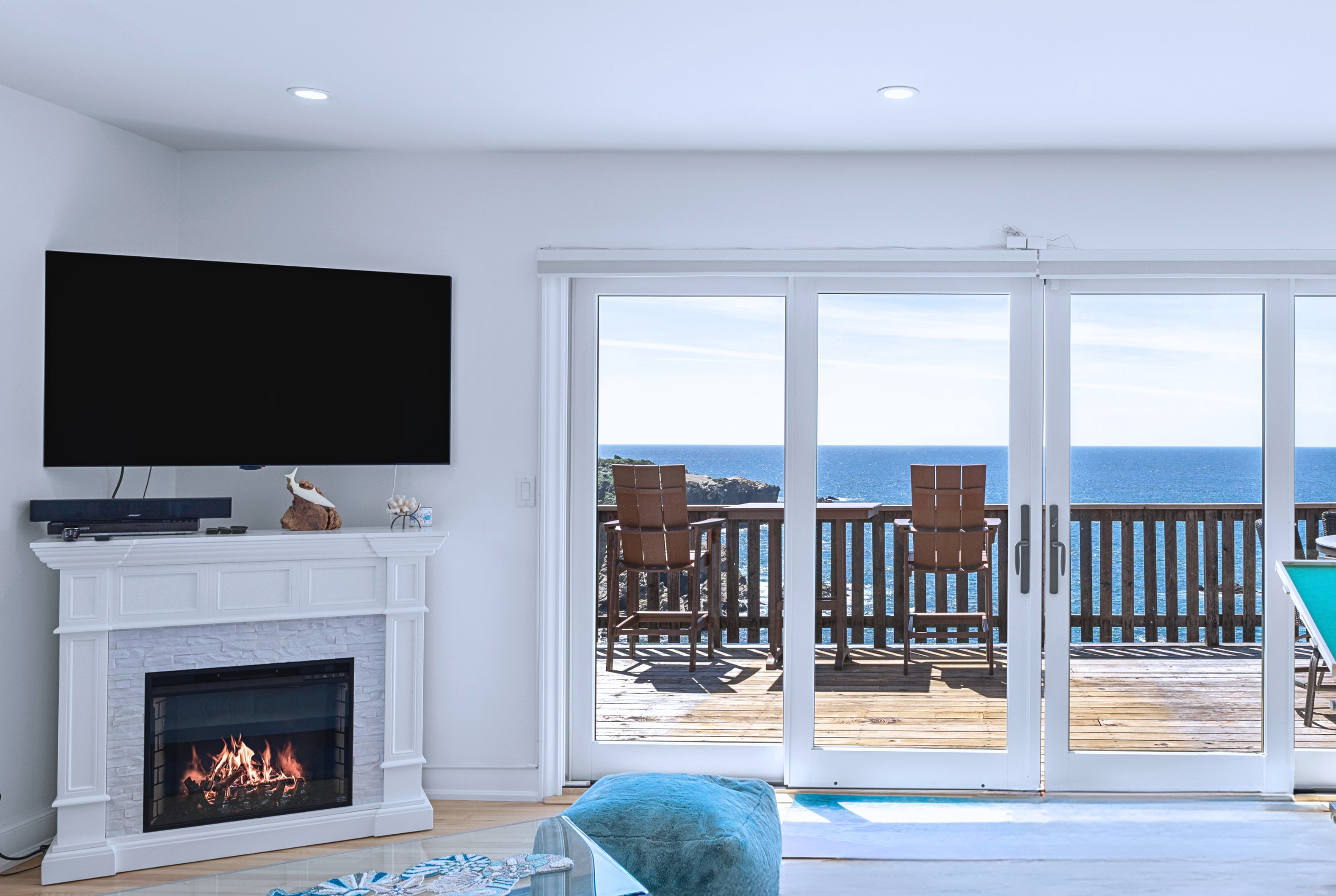 Bright oceanfront lounge with deck seating, fireplace, and big TV