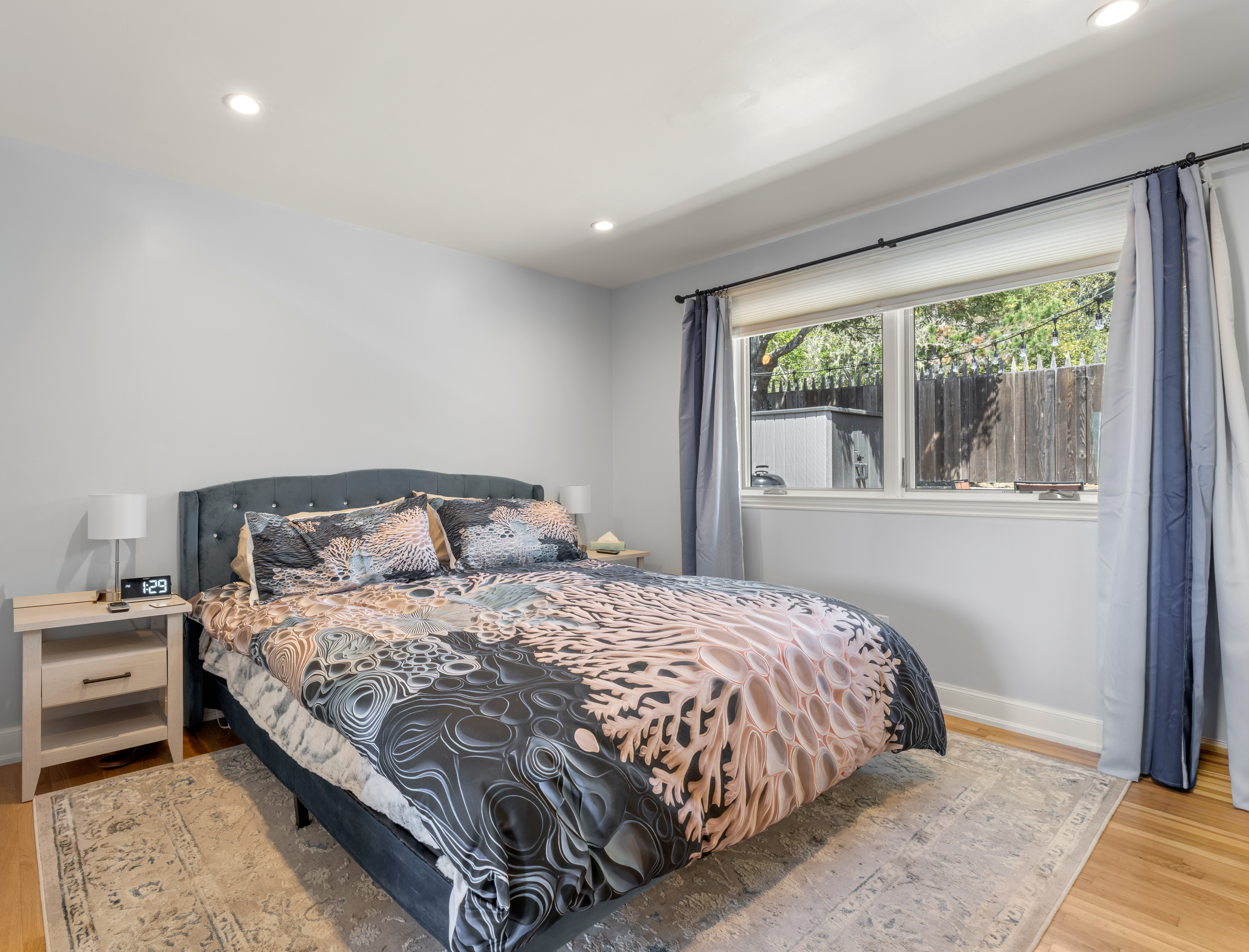 Sunny bedroom with queen bed, tufted headboard, and large window