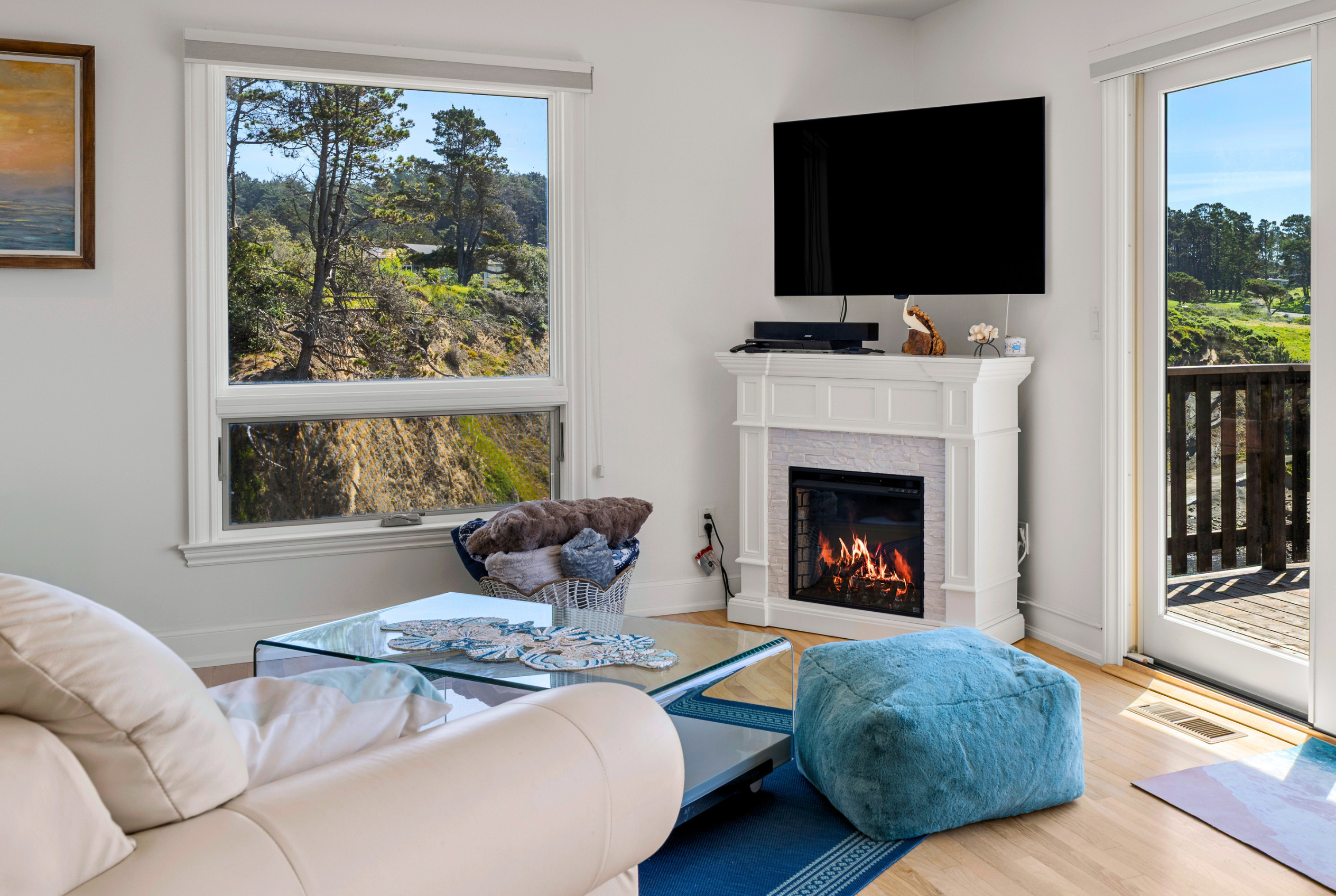Sunny living room with fireplace, TV, and scenic deck views