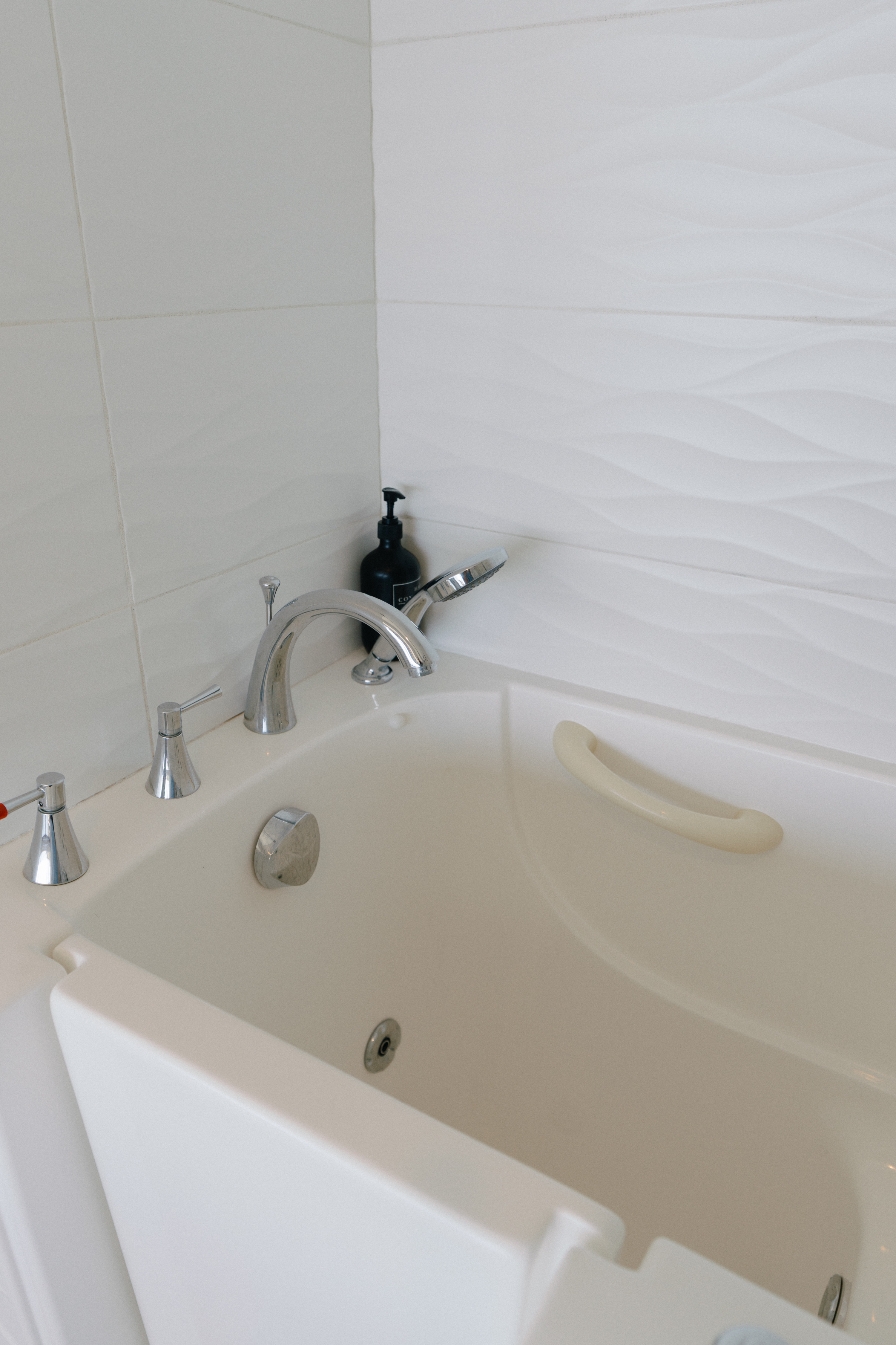 Modern walk-in jetted tub with grab bar and wave-tile surround