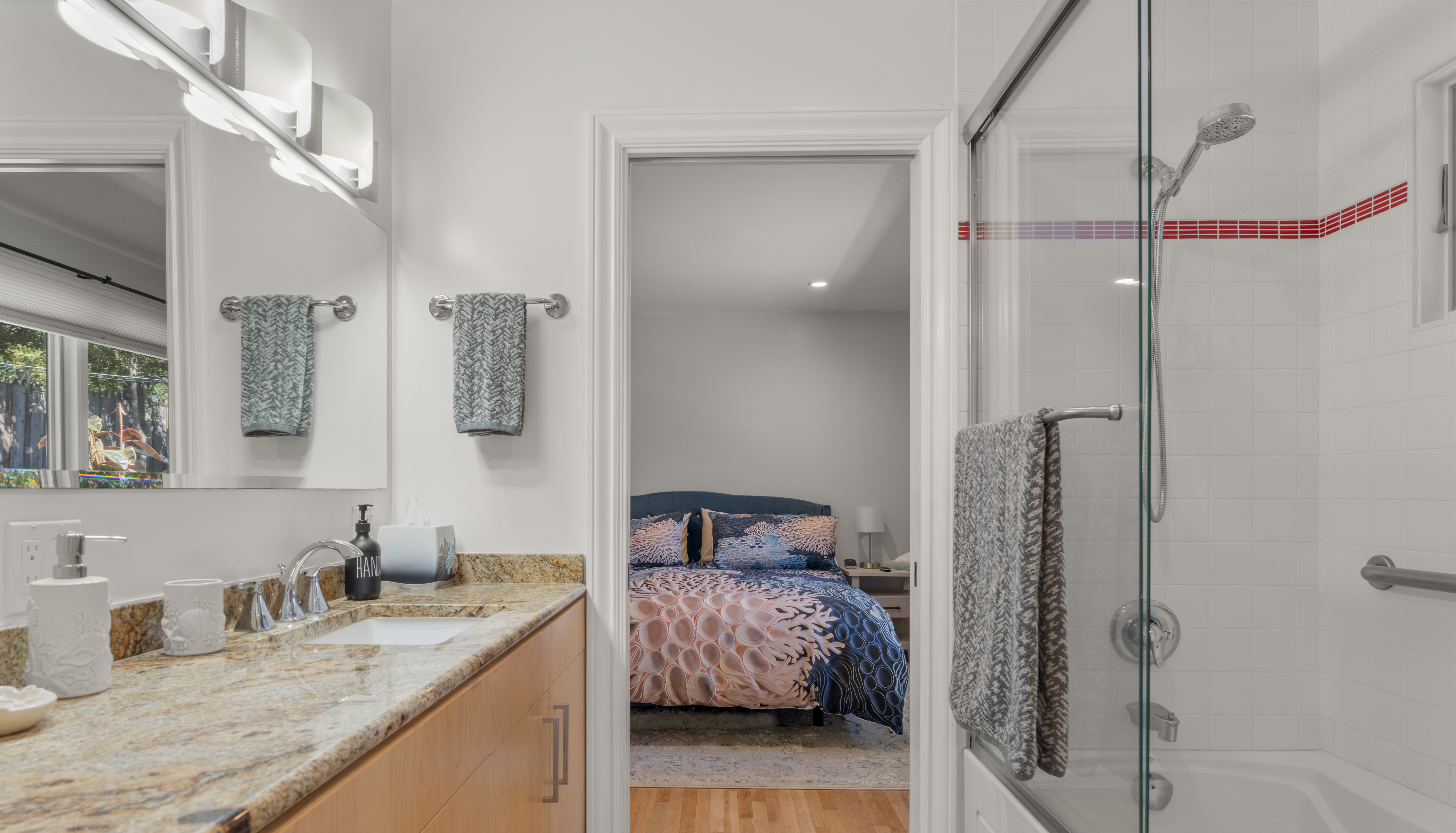Bright bath with double vanity, glass shower, and connected cozy bedroom.