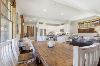 Sunny open-plan farmhouse: rustic dining table, white kitchen, cozy lounge.