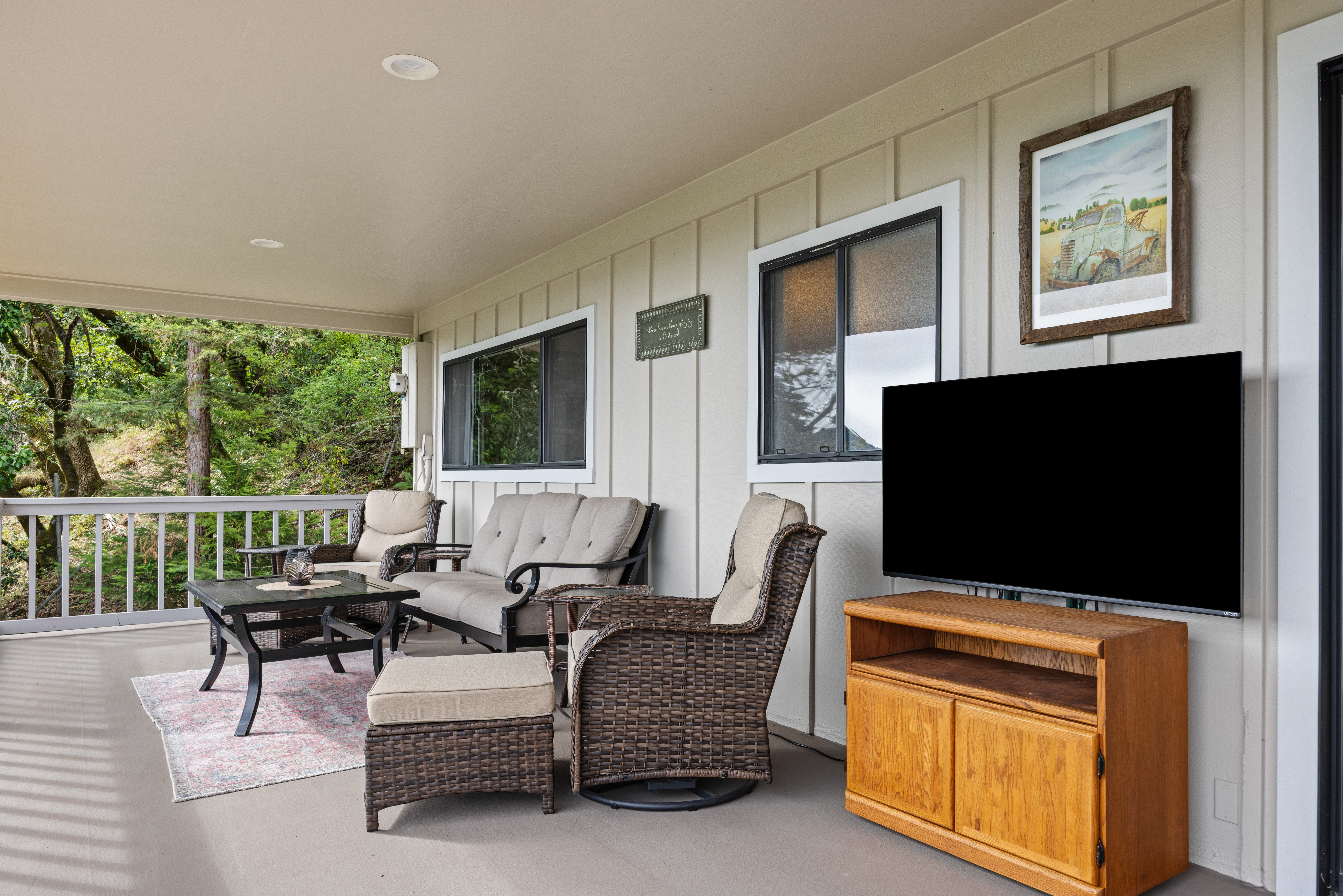 Covered porch with cozy seating, TV, and peaceful wooded views