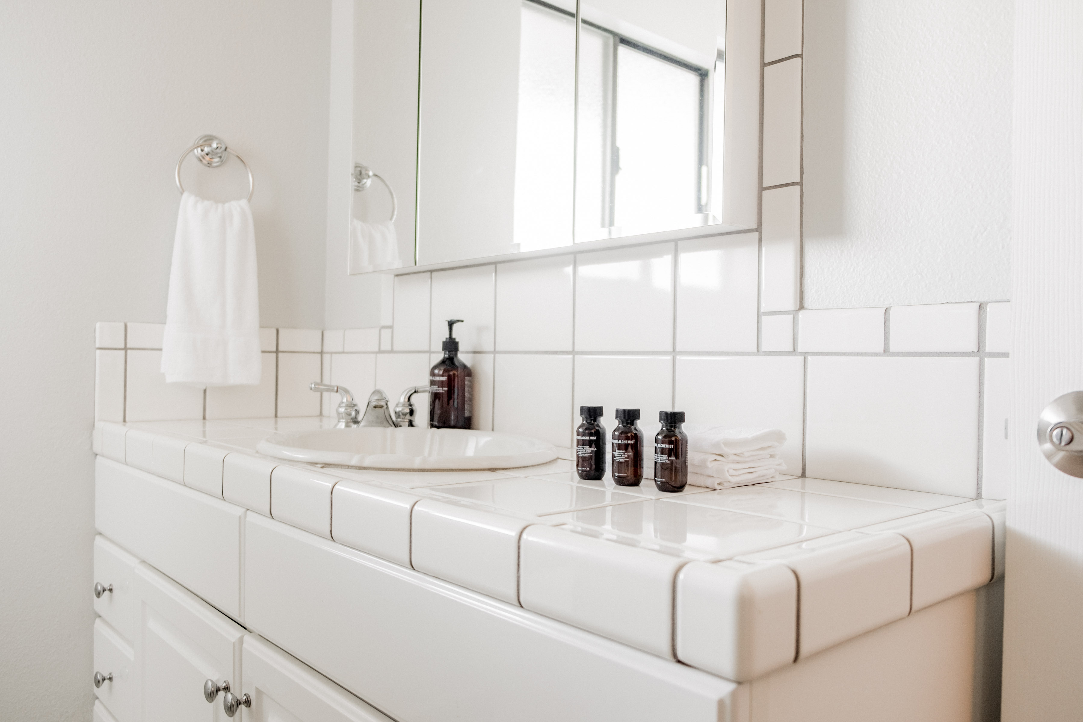Bright tiled bathroom vanity with mirror, fresh towels, and guest amenities