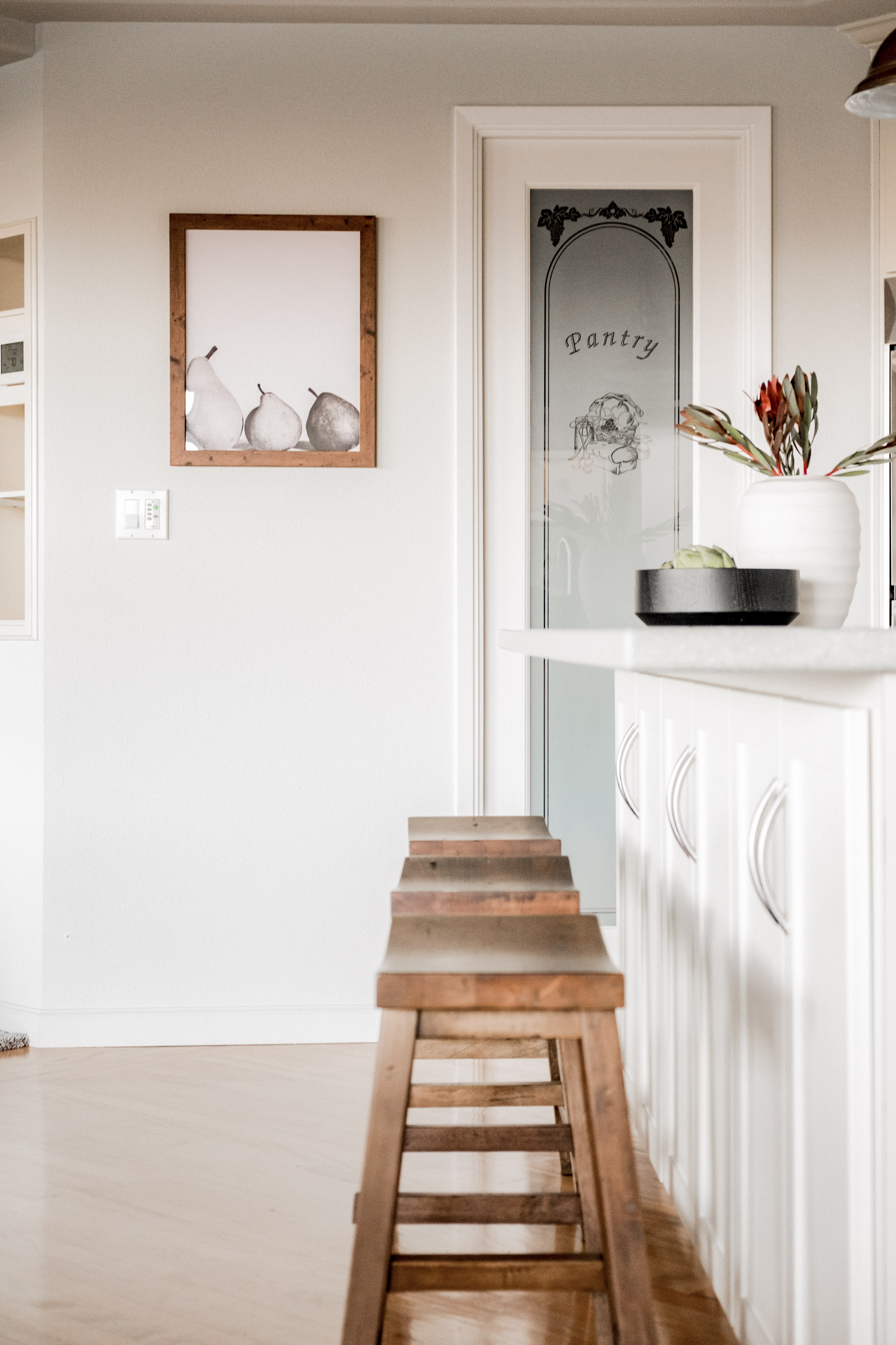 Bright kitchen island with warm wood stools and charming pantry detail