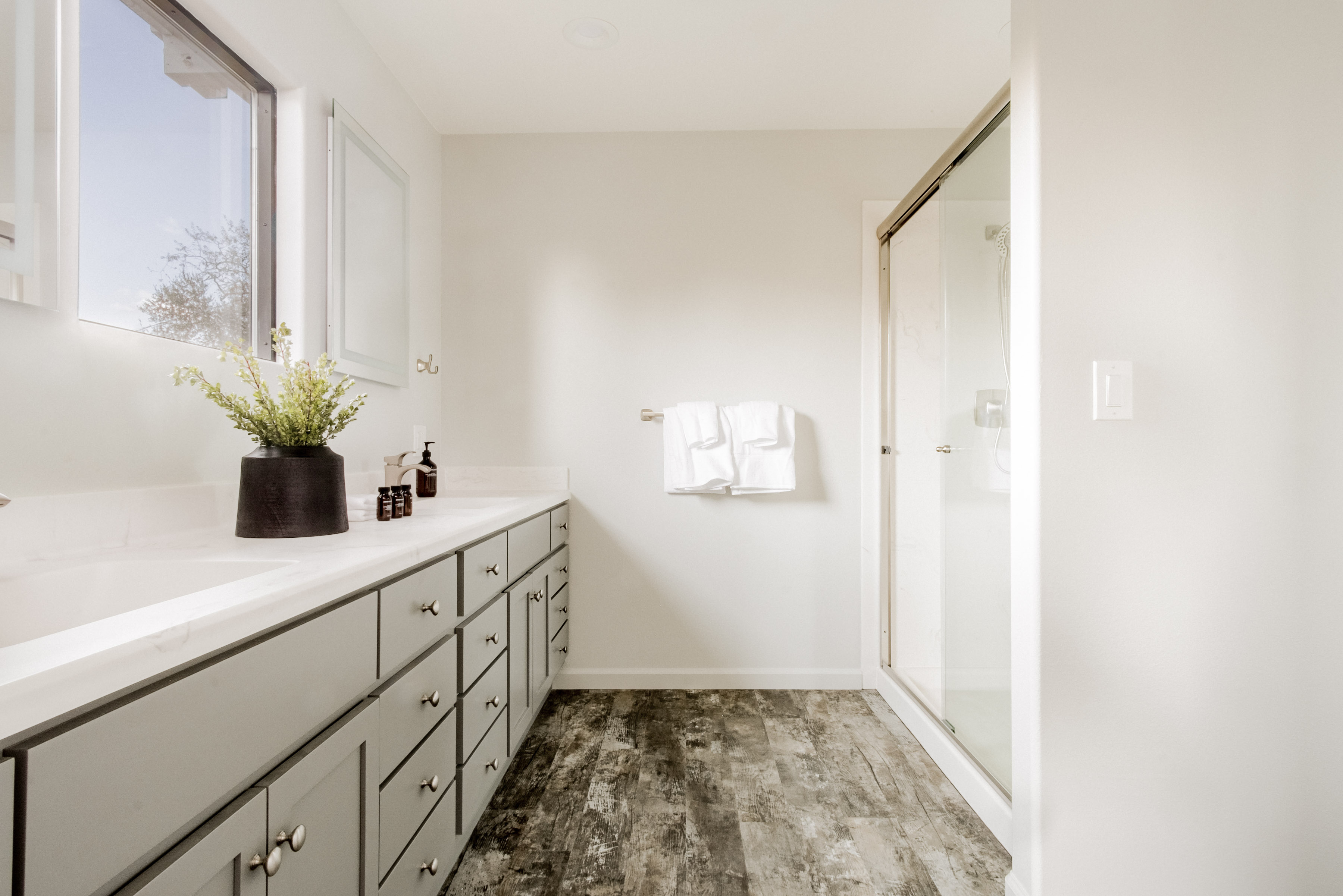 Bright modern bathroom with double vanity, natural light, and glass shower