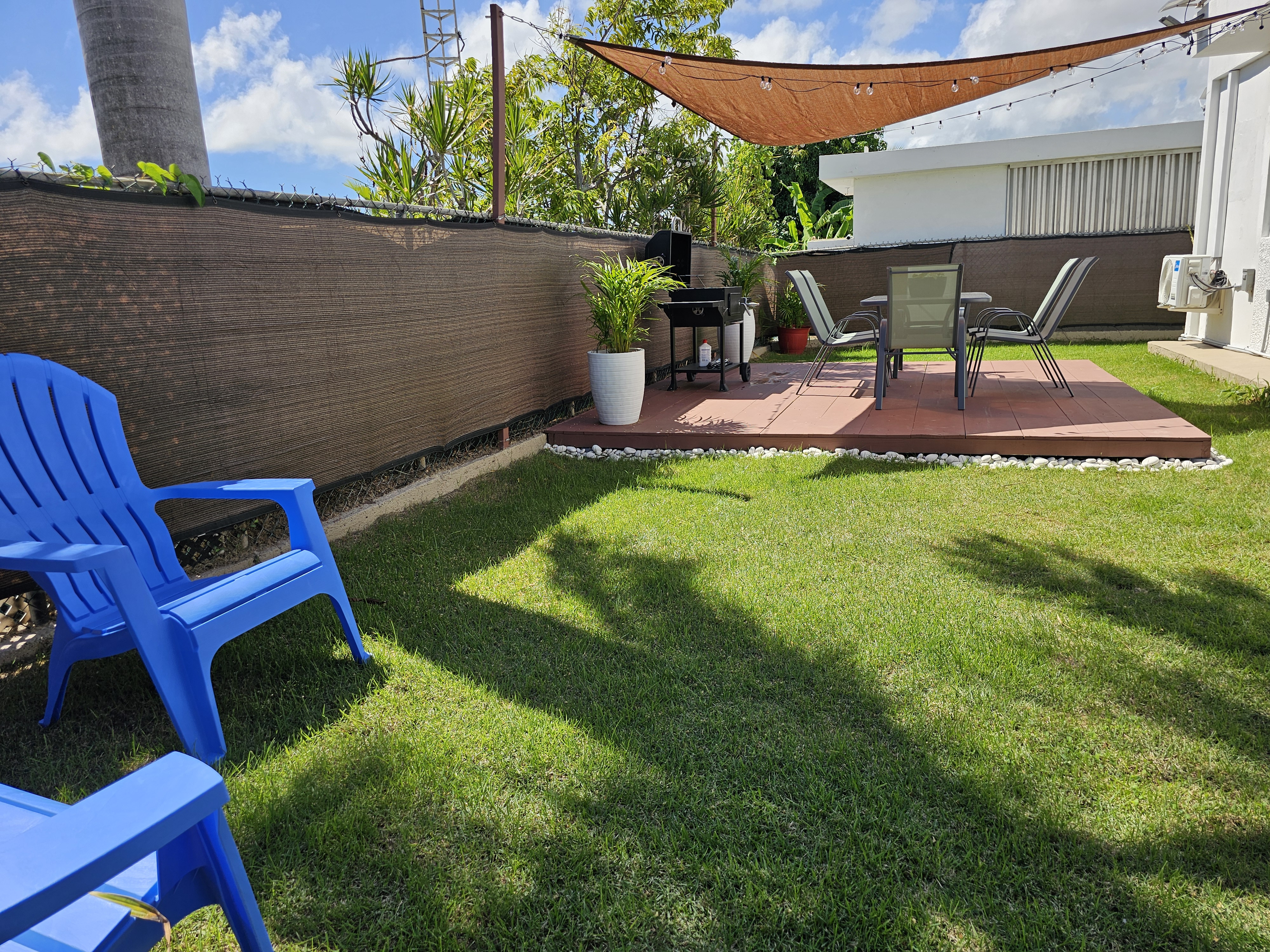 Private backyard patio with grill, loungers, and sunny green lawn